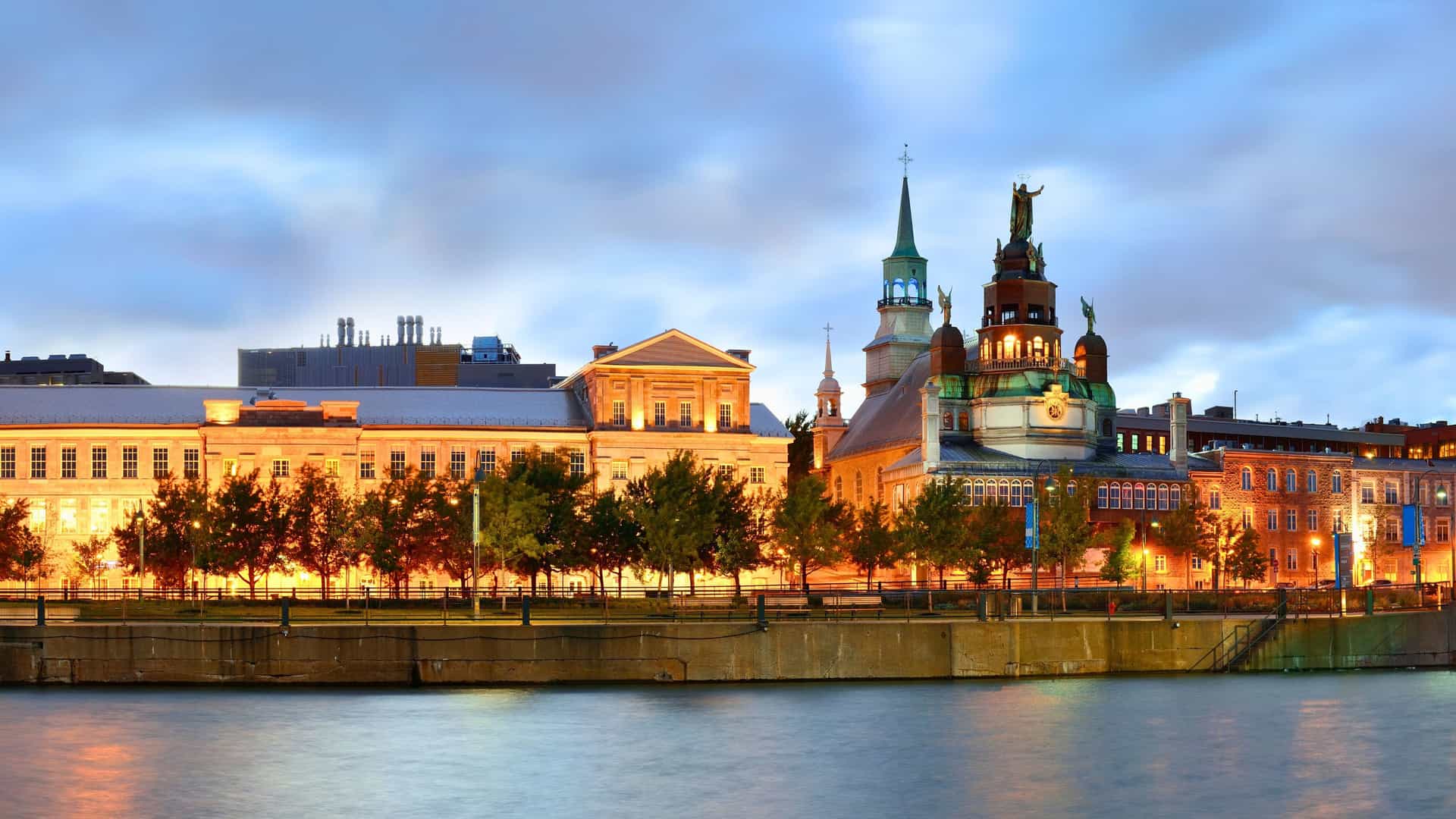 A beautifully lit waterfront view of Old Montreal, Quebec, Canada at dusk, a charming port of call for a luxury Seabourn cruise.