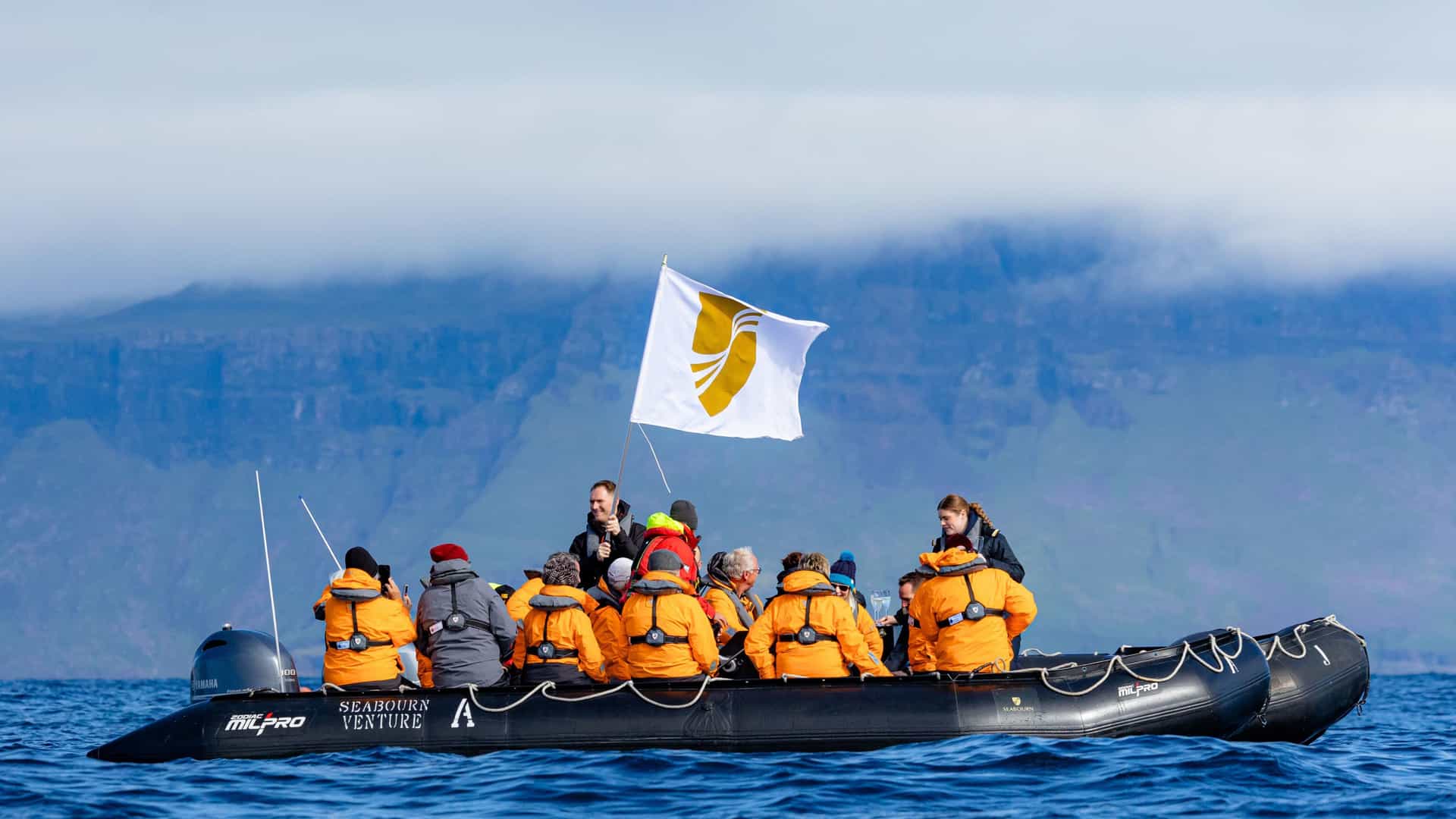 Guests aboard a Seabourn Venture expedition cruise enjoy a scenic Zodiac boat excursion with stunning landscape views.