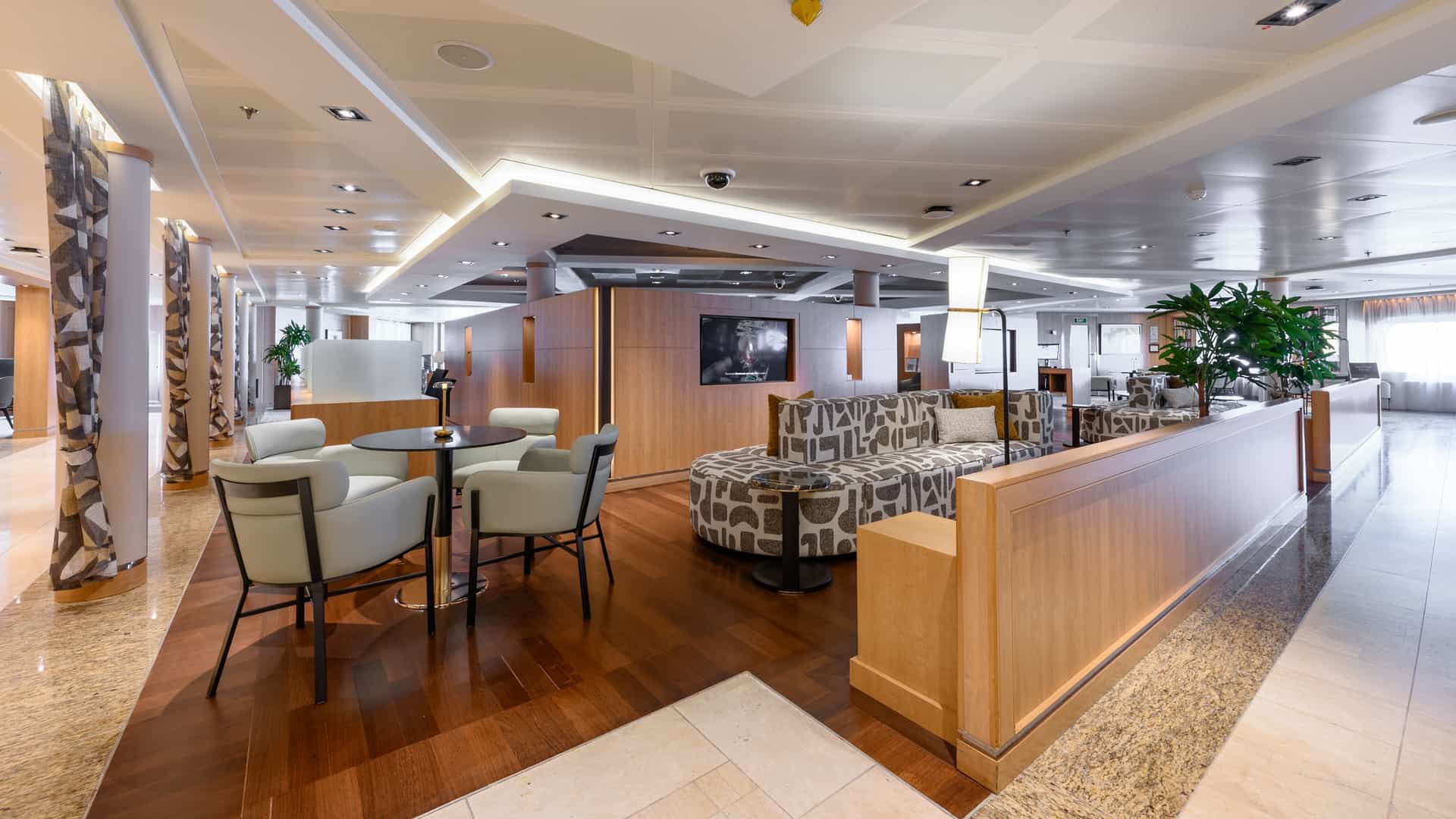 The newly updated Seabourn Square lounge onboard the Seabourn Quest, featuring modern armchairs, a patterned sofa, a small round table, and wooden privacy dividers.