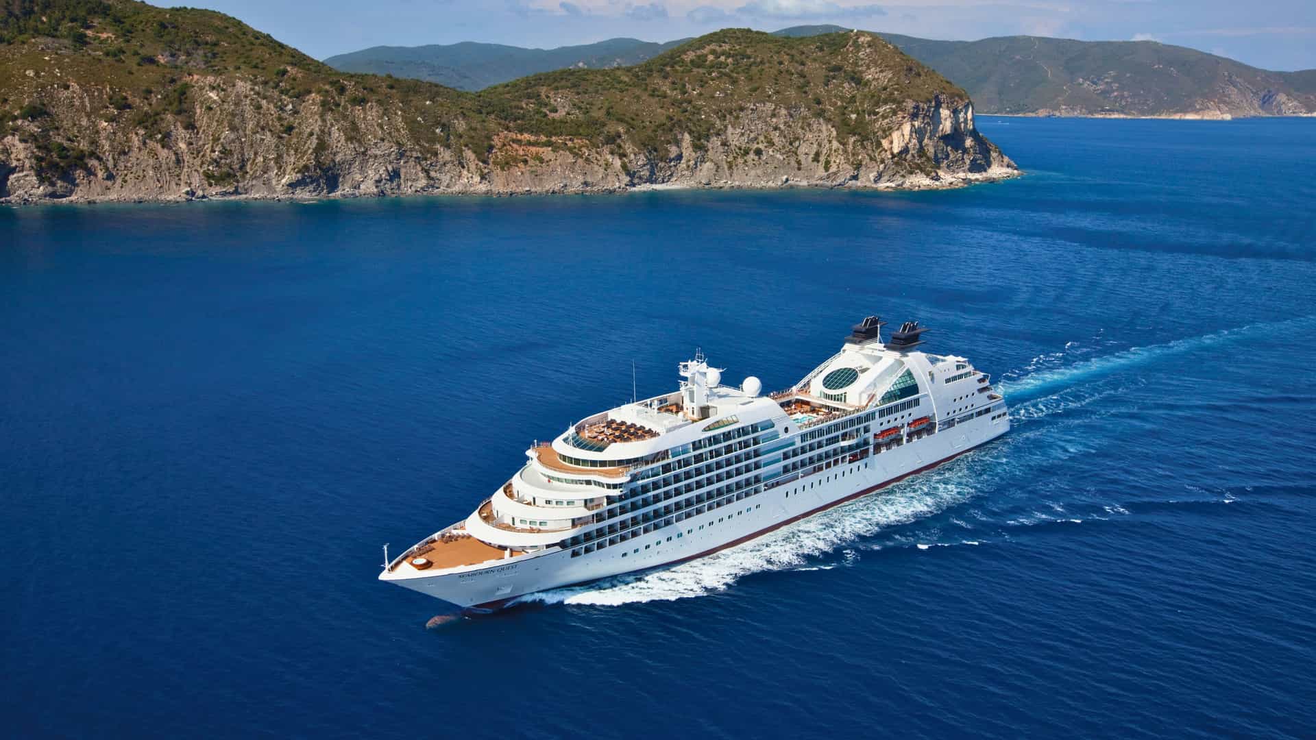 The Seabourn cruise ship sails through the deep blue waters during a Trans-Atlantic crossing, with rugged coastlines visible in the background.