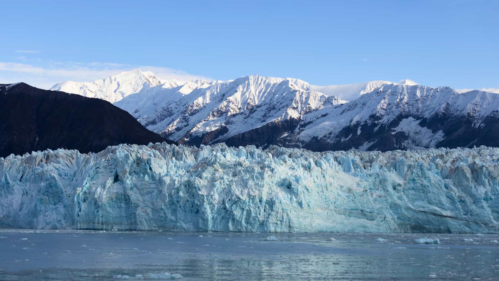 A massive blue glacier meets the ocean with snow-capped mountains in the background on a Silversea cruise in Alaska.