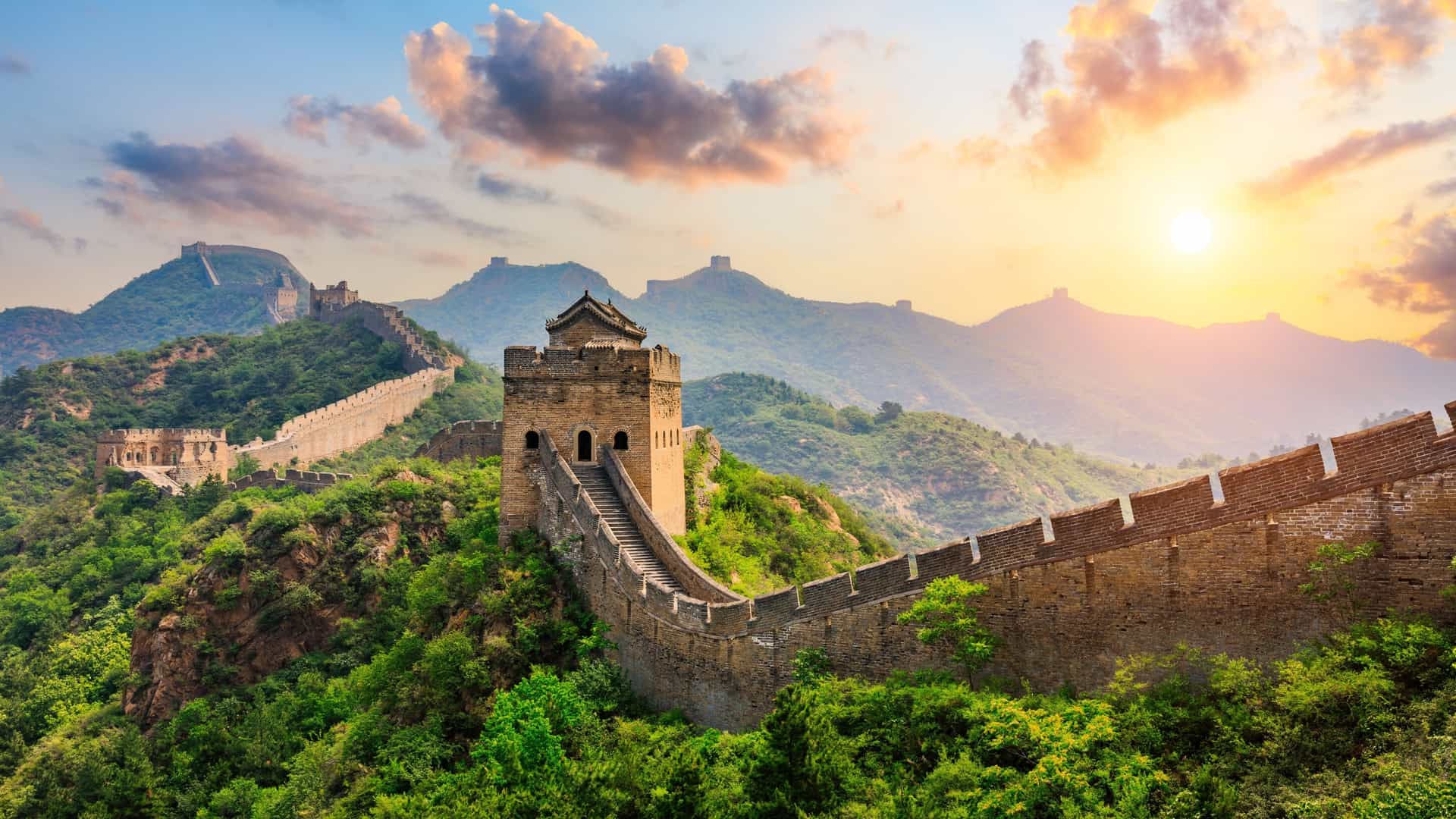 The Great Wall of China winds over lush green hills at sunset, a scenic land excursion on a Silversea cruise.