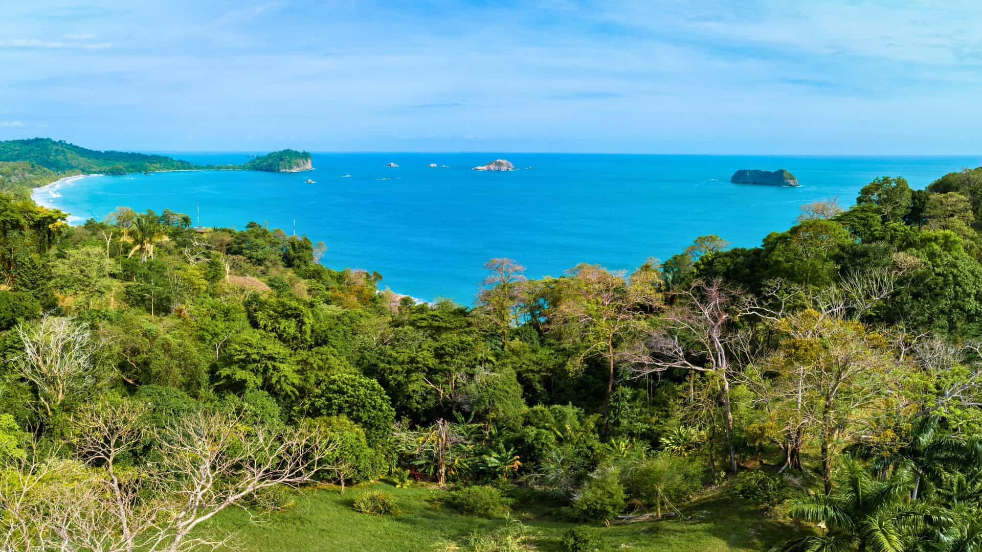 A panoramic view of the coastline at Manuel Antonio National Park, Costa Rica, showing the lush jungle meeting a white-sand beach and the blue ocean, a scenic stop on a Silversea cruise.