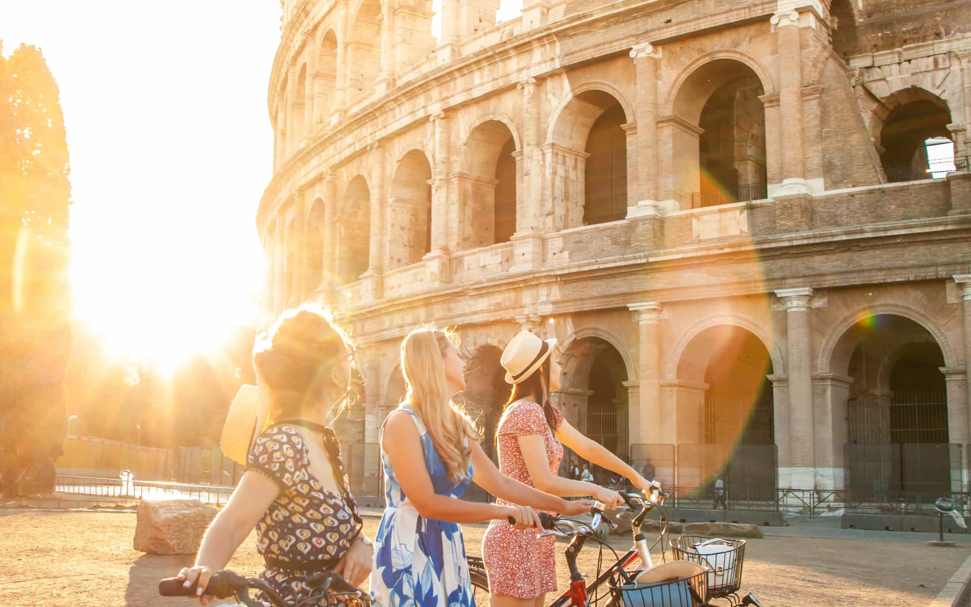 Three woman walking beside their bicycle slowly strolling and admiring the colosseum during golden hour.
