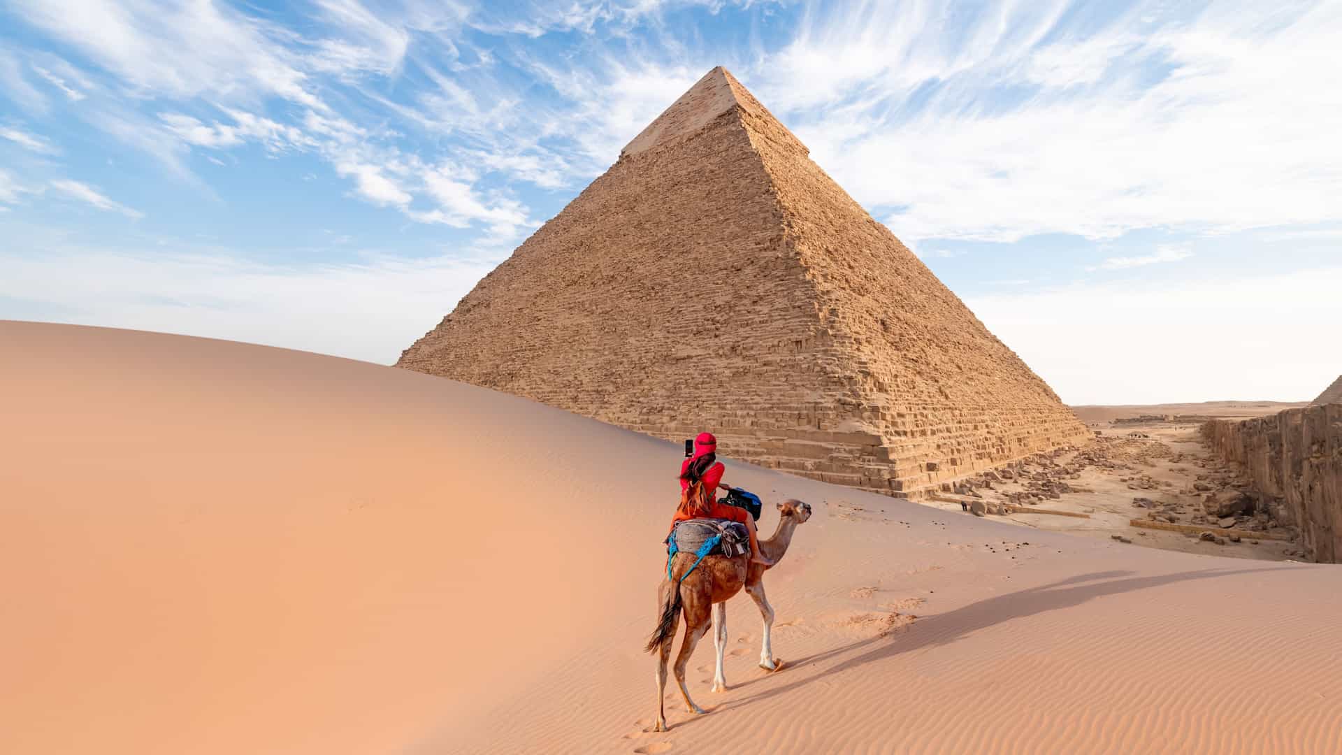 A traveler riding a camel through the desert sand dunes with the ancient Giza pyramids in Egypt on a Tauck tour.