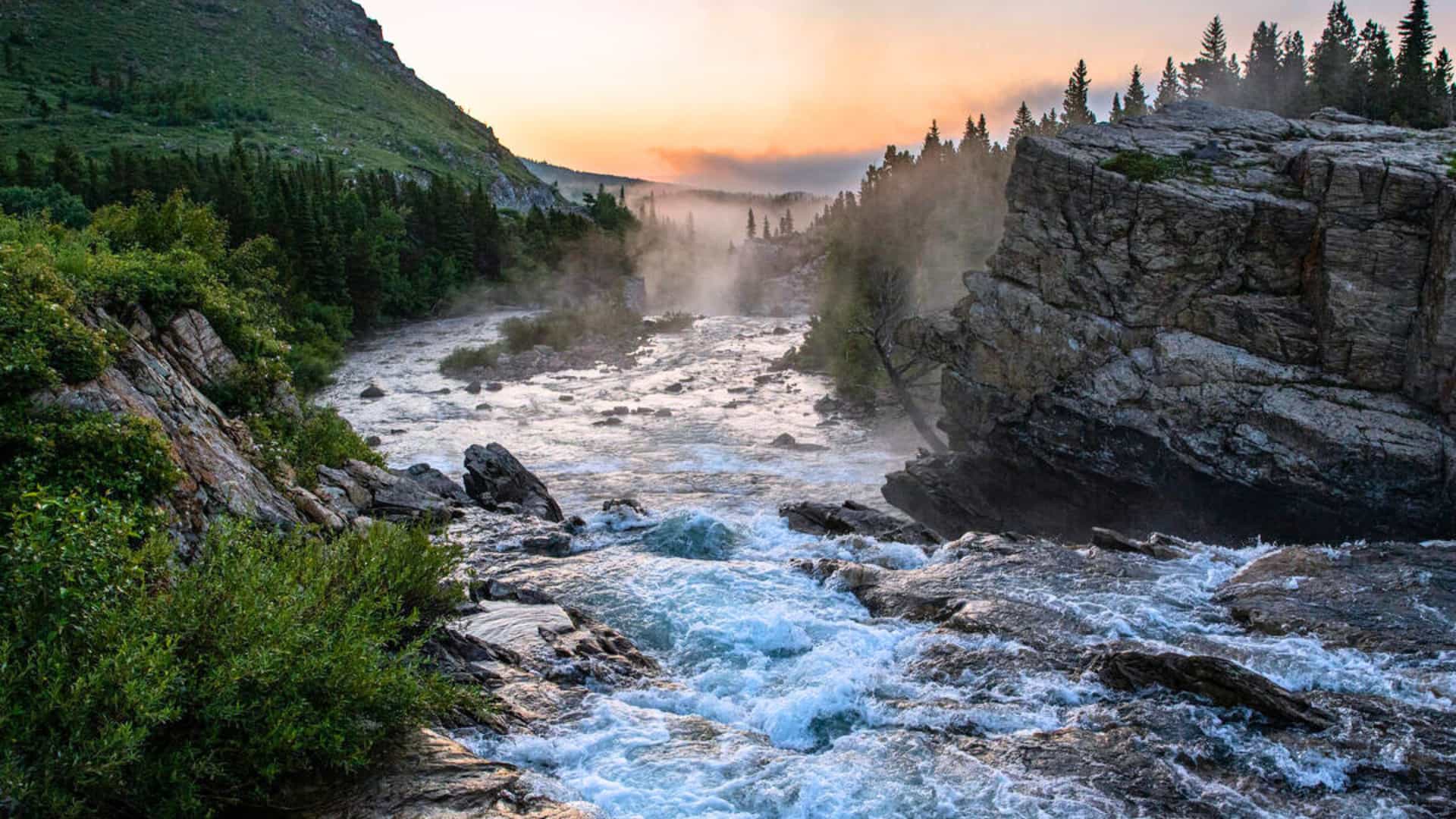 Tauck land tour landscape at Swift Current Lake, Glacier National Park with misty river, forest cliffs, and sunrise glow