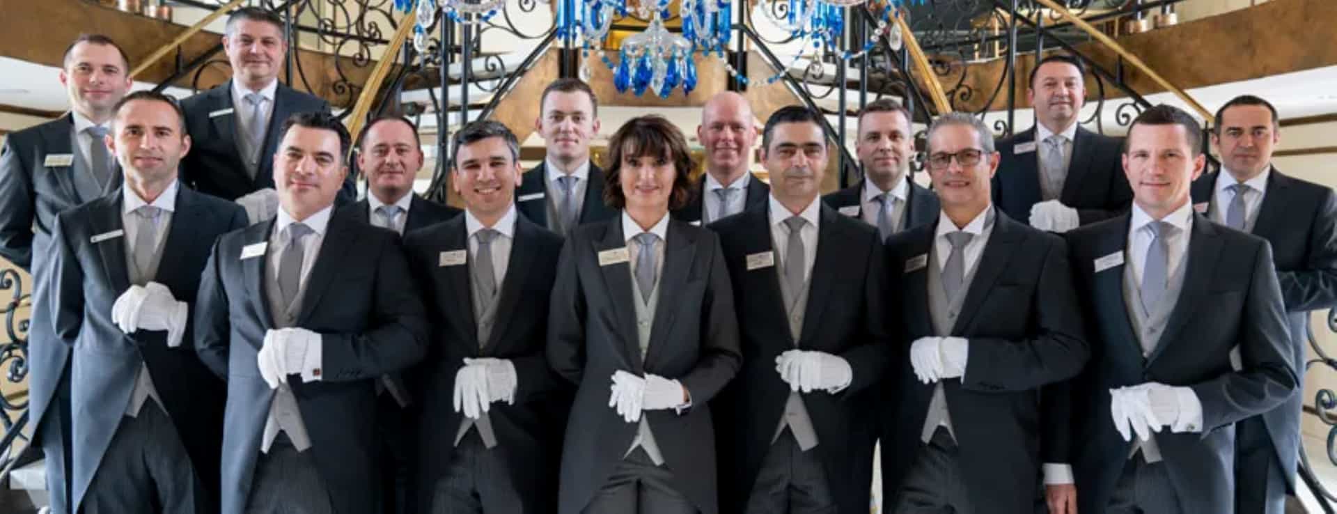 A group of butlers standing tall together in front of a double split staircase onboard a Uniworld river cruise ship.