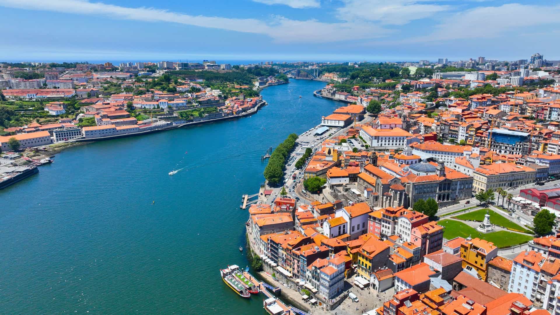 An aerial view of the Douro River flowing through a historic city, with colorful buildings and red-tiled roofs lining the riverbanks, showcasing the vibrant cityscape of a Uniworld river cruise destination in Portugal.