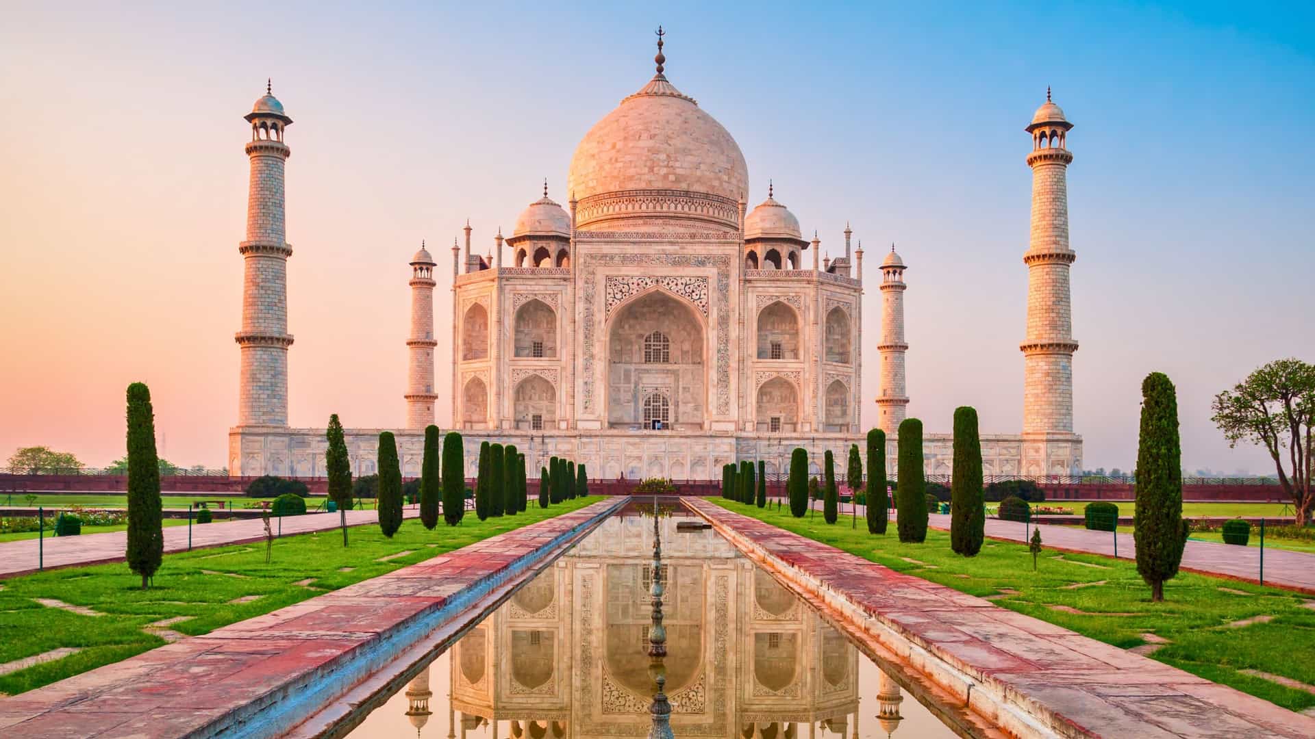 The majestic Taj Mahal in Agra, India, is perfectly reflected in a long reflecting pool at sunrise. This iconic monument is a key river cruise destination on a Uniworld luxury tour.