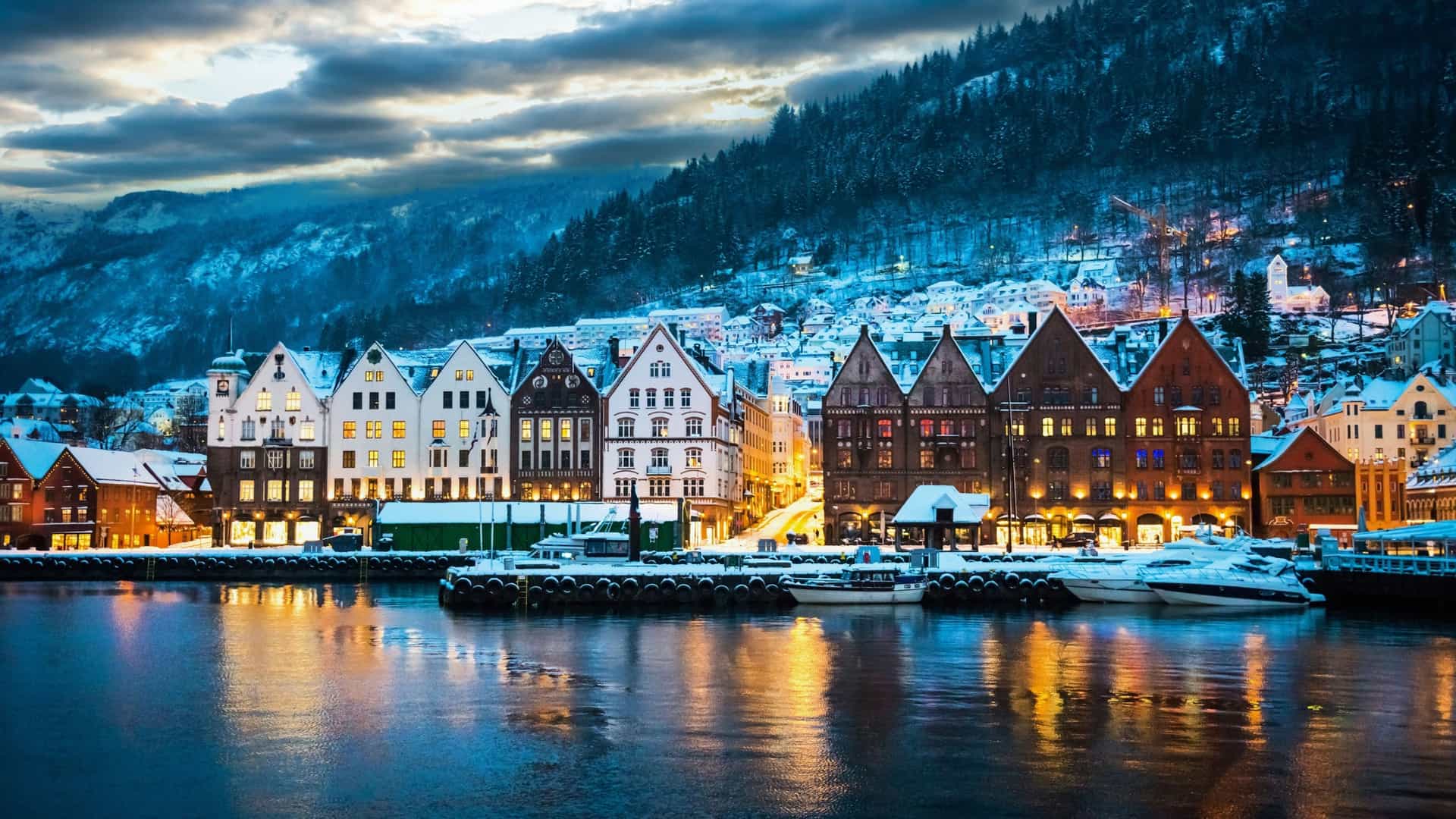 Snow-covered waterfront in Bergen, Norway, with colorful historic buildings reflecting in the harbor—an enchanting stop on Viking Expedition Cruises through Northern Europe.