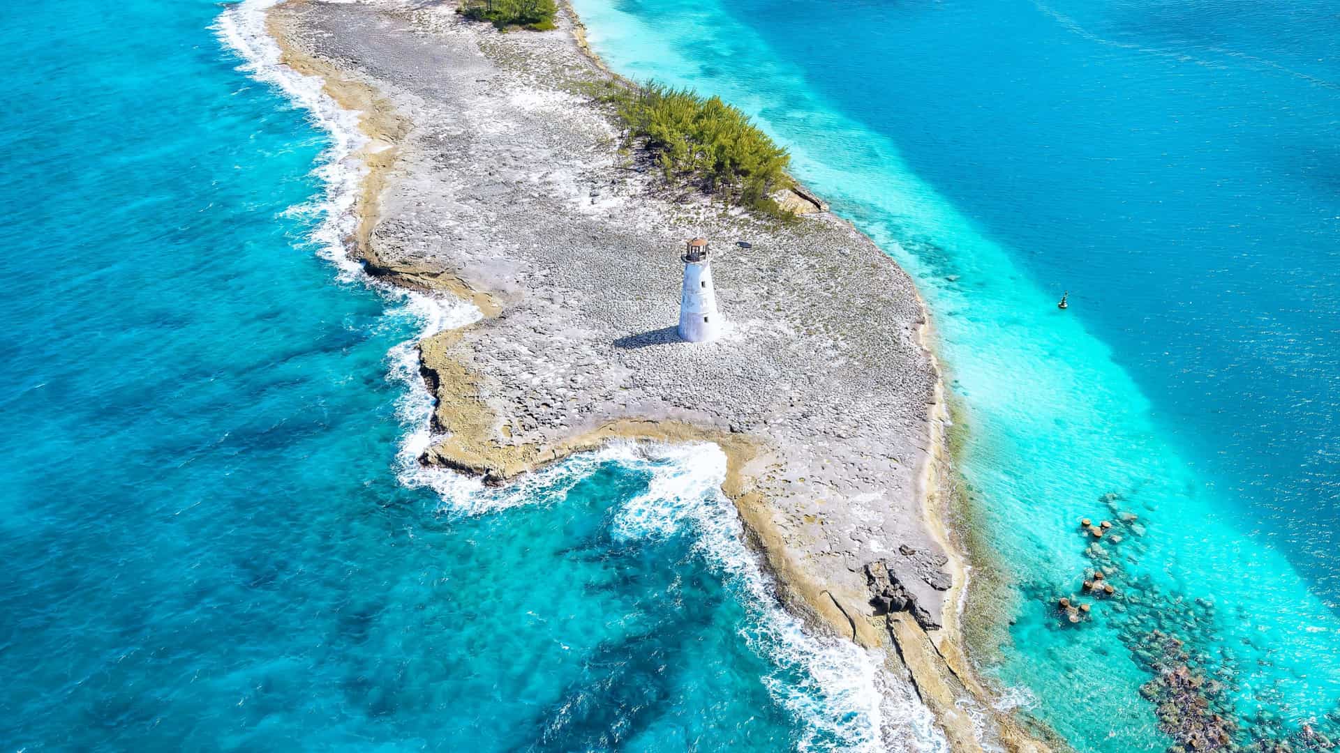 An aerial view of a small island with a white lighthouse surrounded by turquoise water in the Bahamas, a Windstar cruise destination.