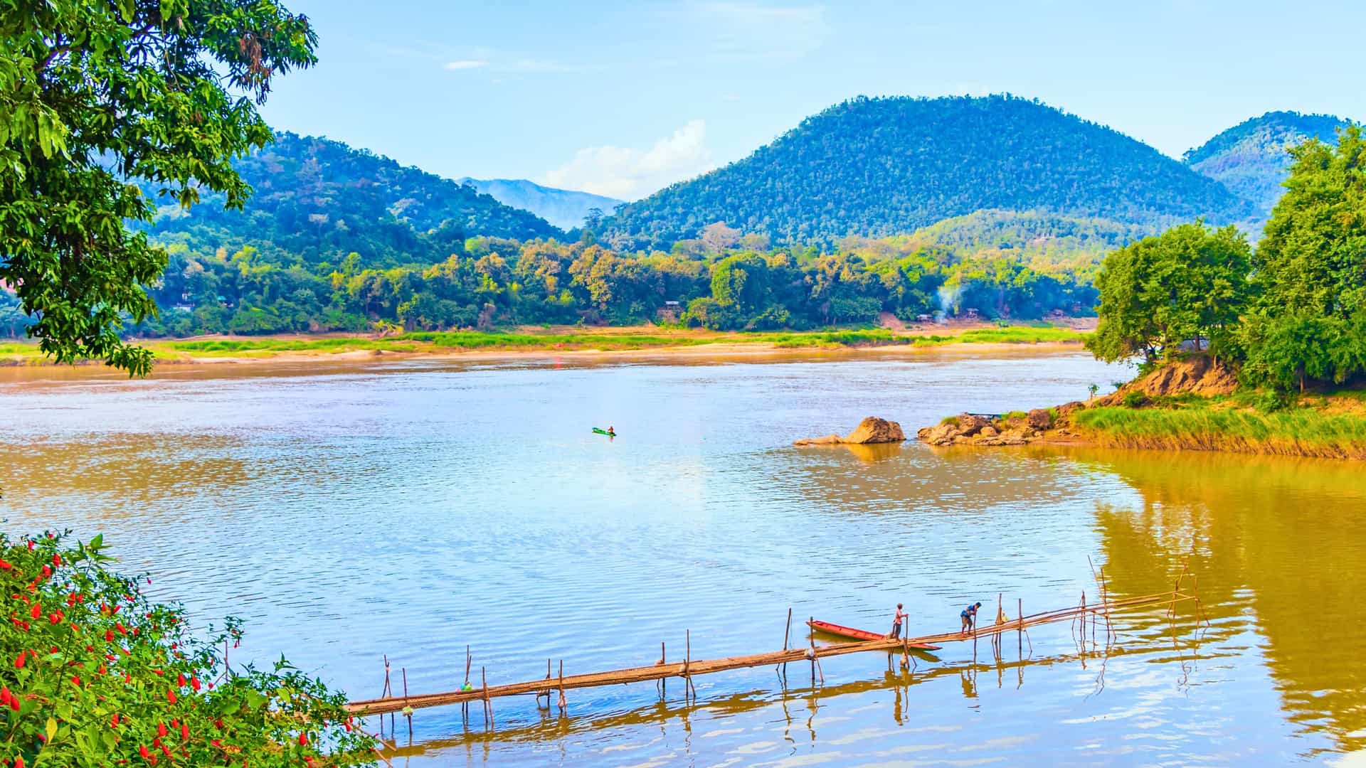 Scenic view of the Mekong River with lush mountains and a wooden bridge, a destination for a Windstar cruise in Southeast Asia.