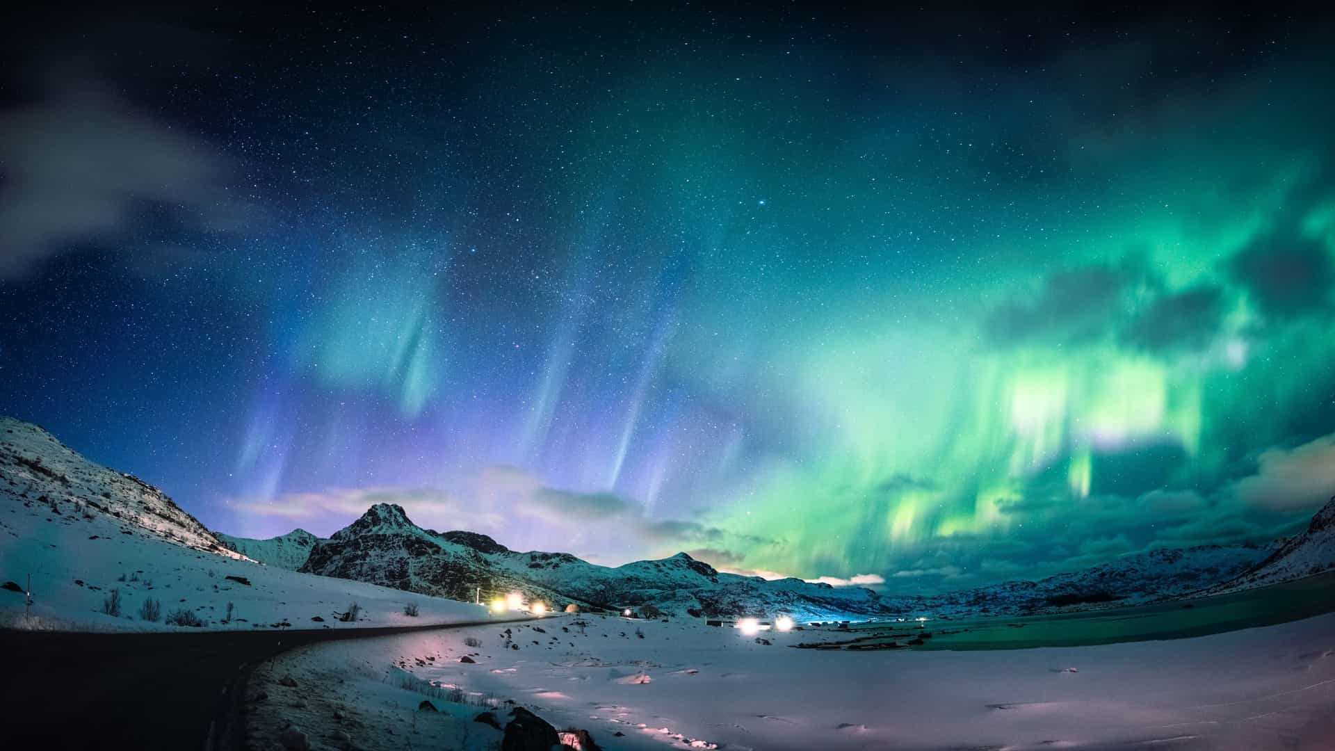 Vibrant Aurora Borealis dancing over a snowy landscape in the Arctic Circle, a Windstar cruise experience.