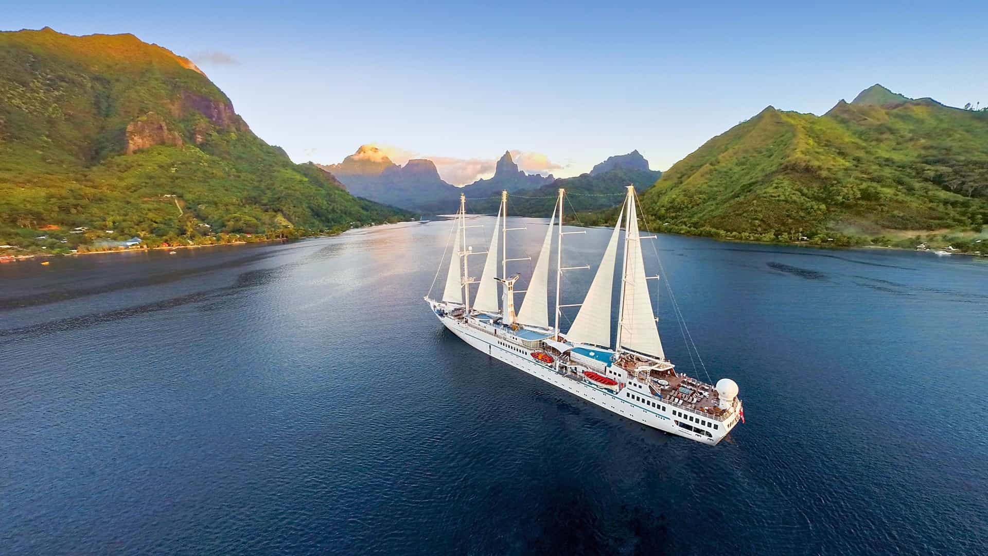 An aerial view of a Windstar cruise sailing ship in a tropical bay surrounded by green mountains in Moorea, a highlight of a trans-pacific cruise.