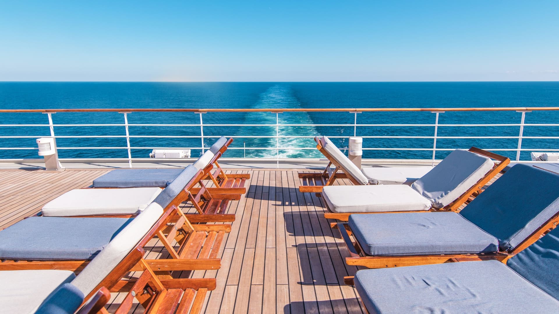 Two rows of lounge chairs on a cruise ship deck during a bright, sunny day.