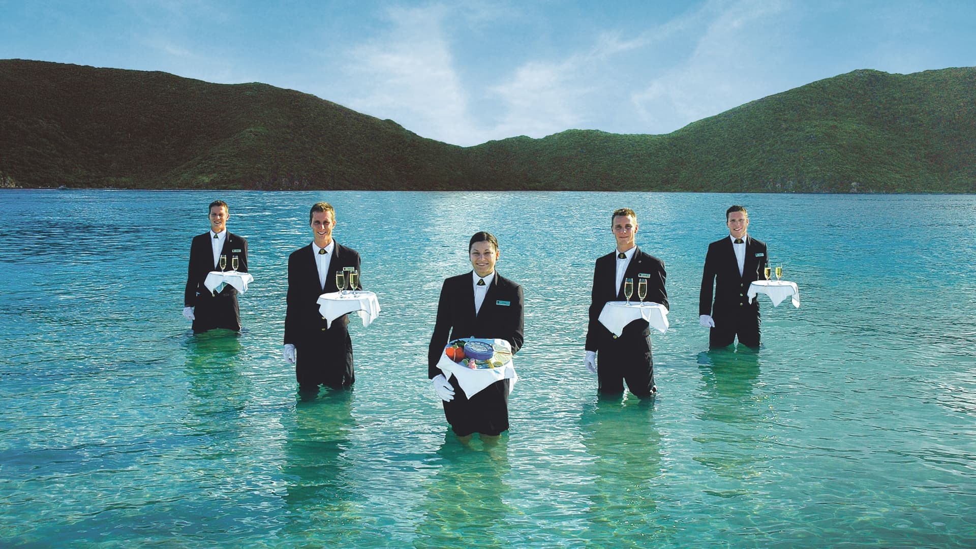 Five members of Seabourn's staff in suits standing in the water holding trays for the signature Caviar in the Surf event.