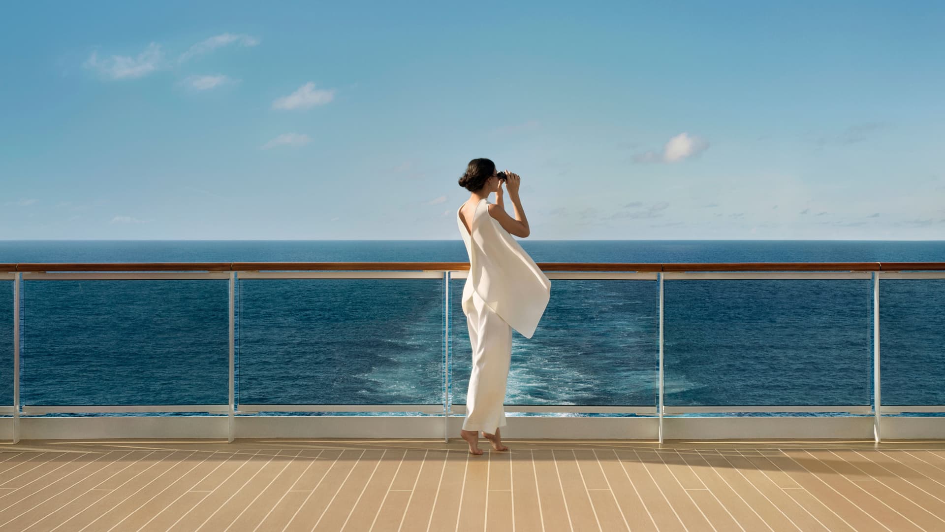 A woman wearing all white using binoculars to view the ocean.