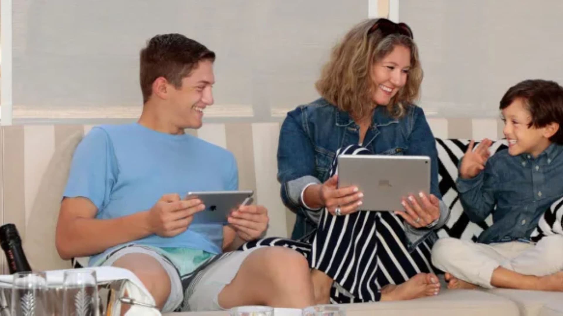 A family using iPad tablets on a couch aboard a cruise ship with a bucket of iced drinks in the foreground.