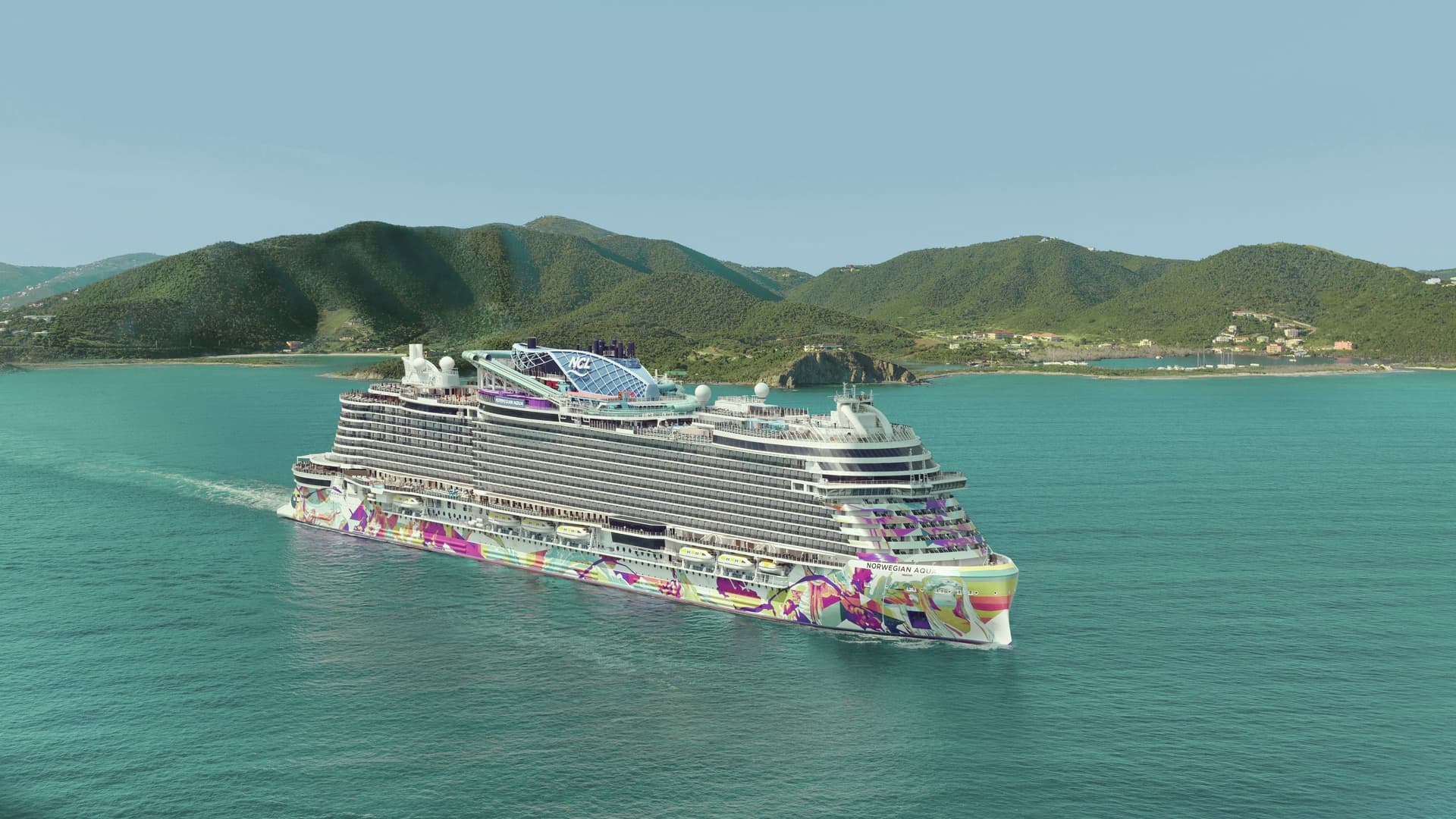 Aerial shot of Norwegian Aqua sailing through Tortola with grassy mountains in the background and a clear blue sky.