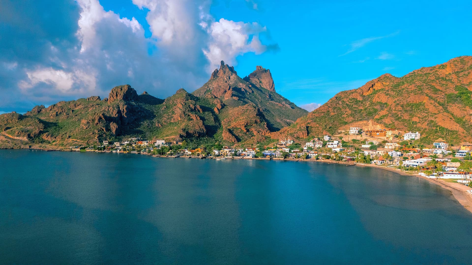 An aerial view of the scenic bay and coastal community in Guaymas, Mexico, with rugged mountains and a beautiful blue sky in the background.