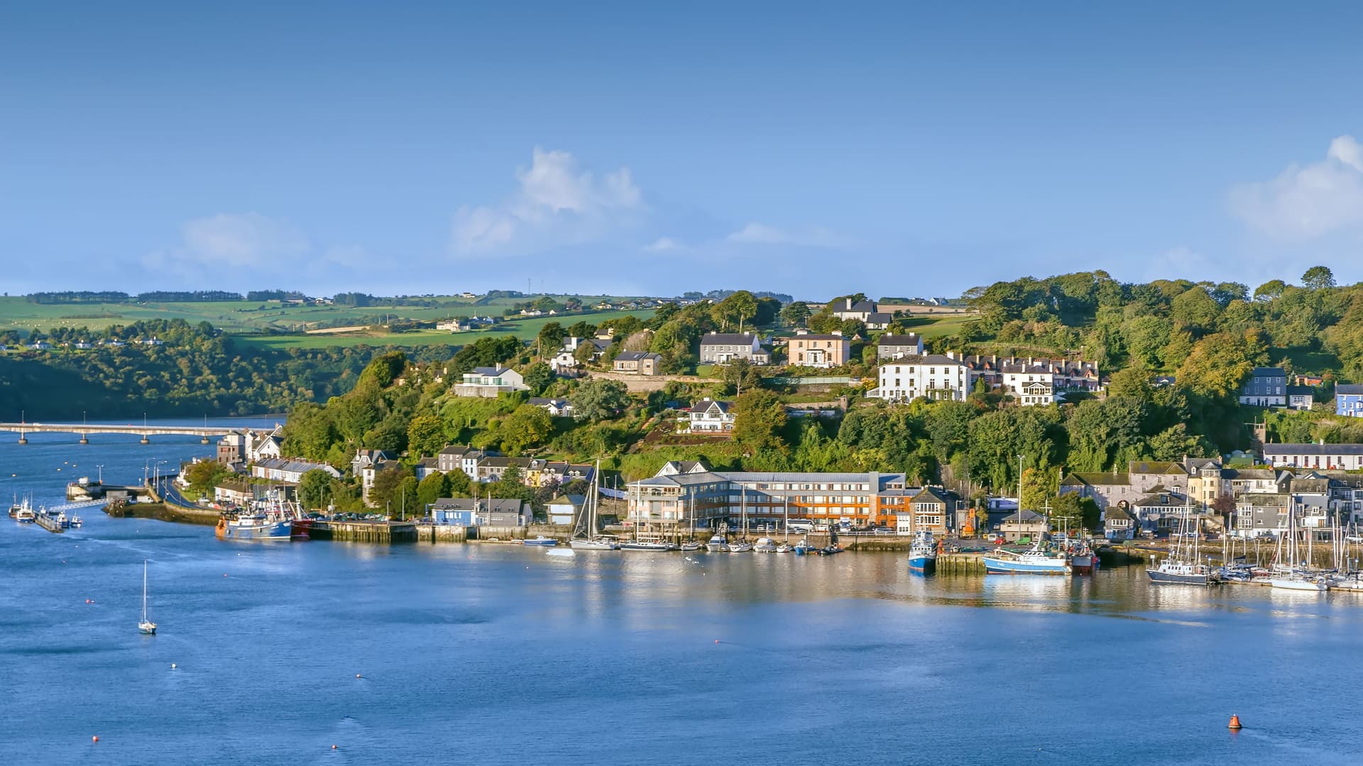 "A beautiful harbor shot of the coastal town of Kinsale, Ireland, with colorful buildings and houses lining the steep hills overlooking the calm water, with boats and yachts moored in the marina.  "