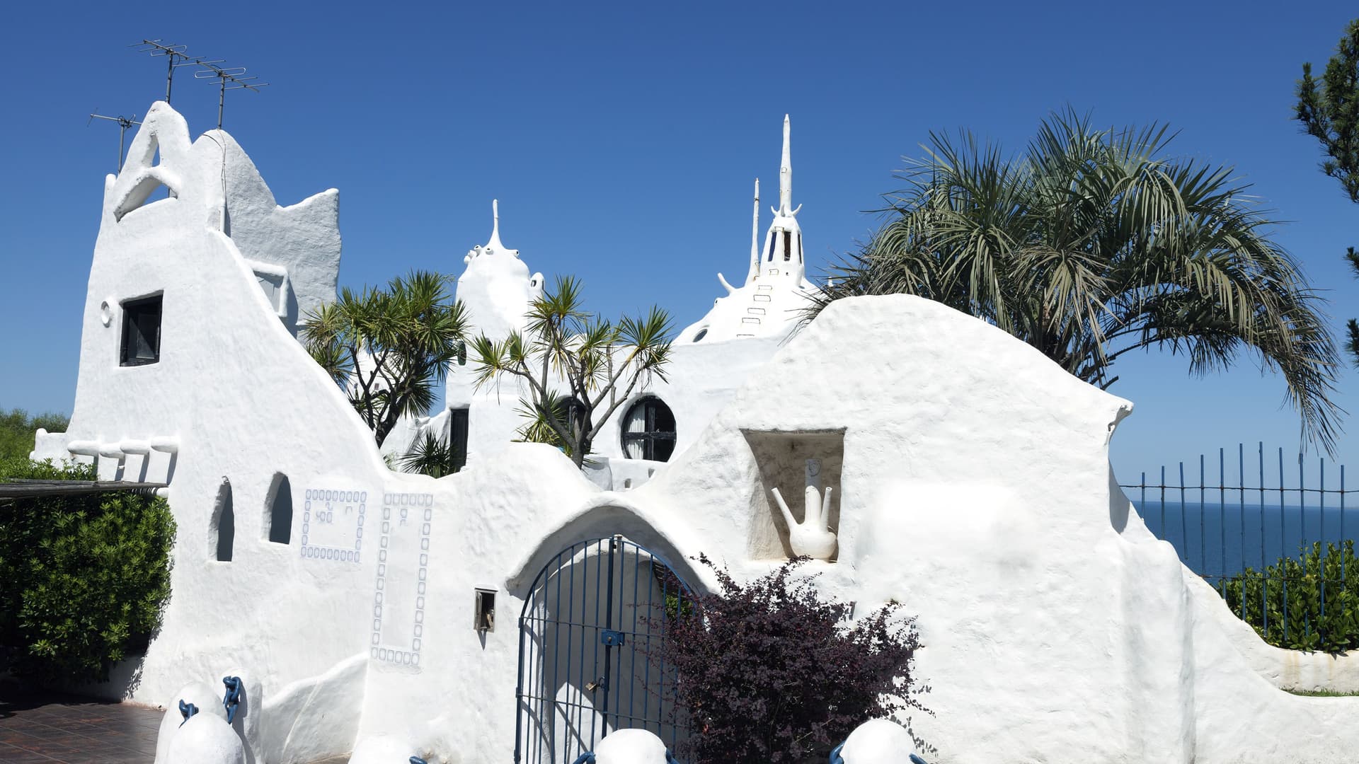 A unique architectural close-up of Casapueblo, a white plaster Mediterranean-style villa and museum built by Carlos Páez Vilaró on the cliffs of Punta del Este, Uruguay, against a clear blue sky.