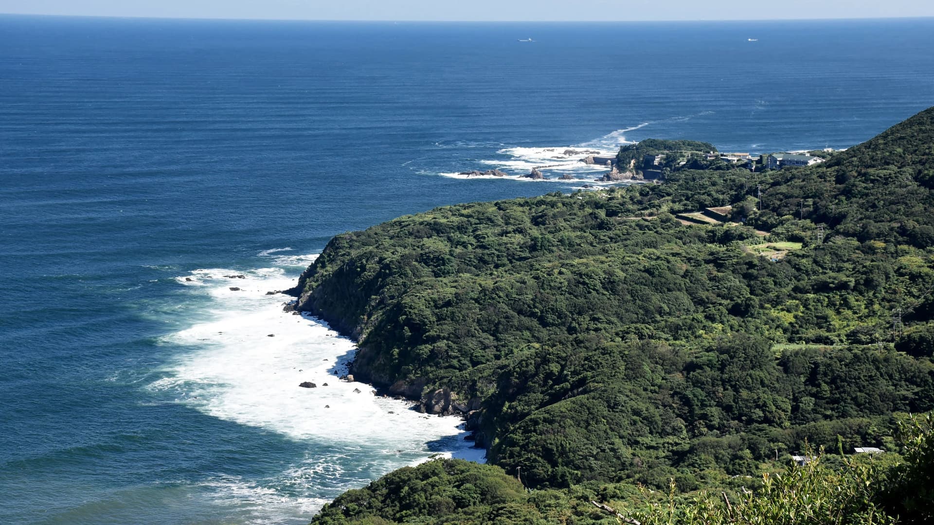 A beautiful aerial view of the rugged coastline of Toba, Japan, with green forested cliffs meeting the deep blue ocean.