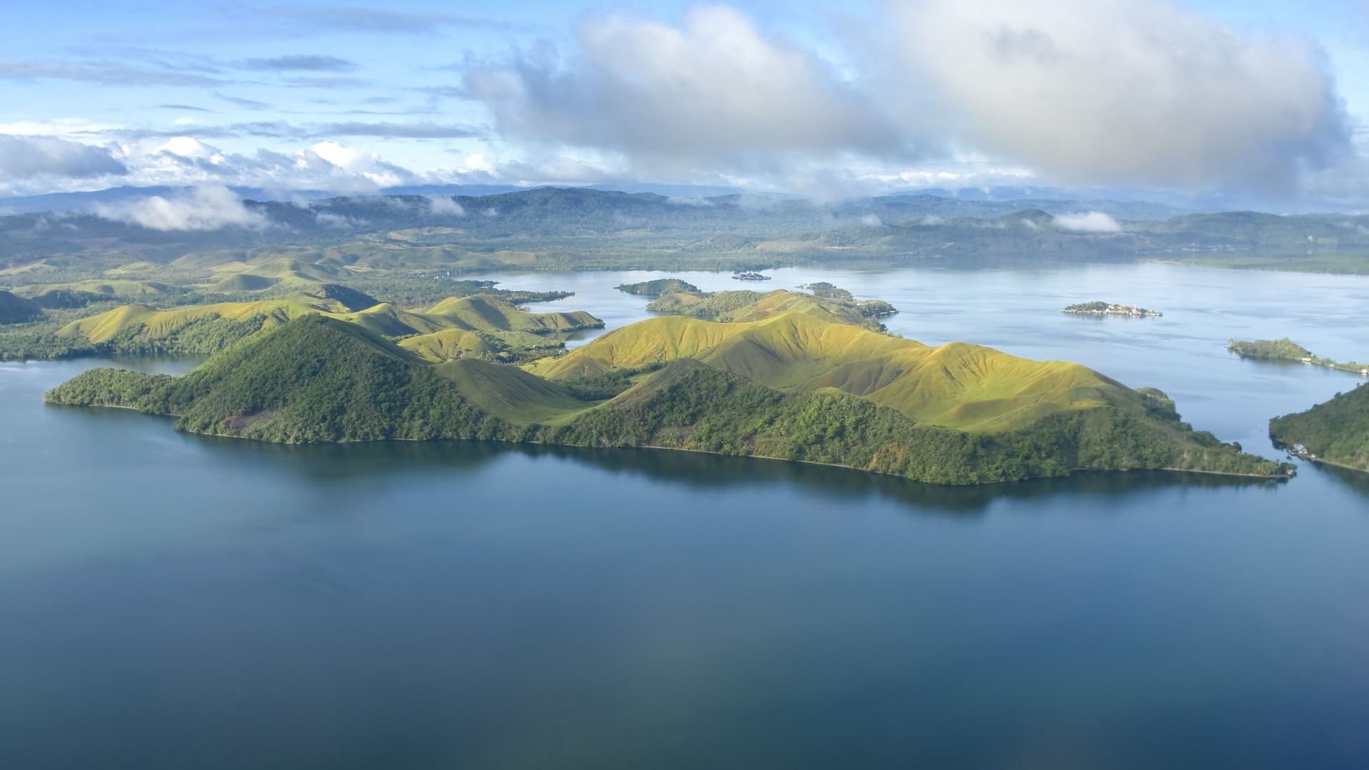 An aerial view of the verdant, rolling hills and a peninsula jutting out into the deep blue waters of Vanimo, a picturesque coastal town in Papua New Guinea.