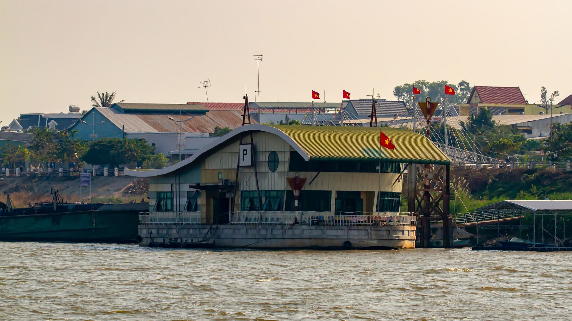 A view of a floating building with Vietnamese flags, serving as a border crossing point on the river between Vietnam and Cambodia, with other structures visible in the background.