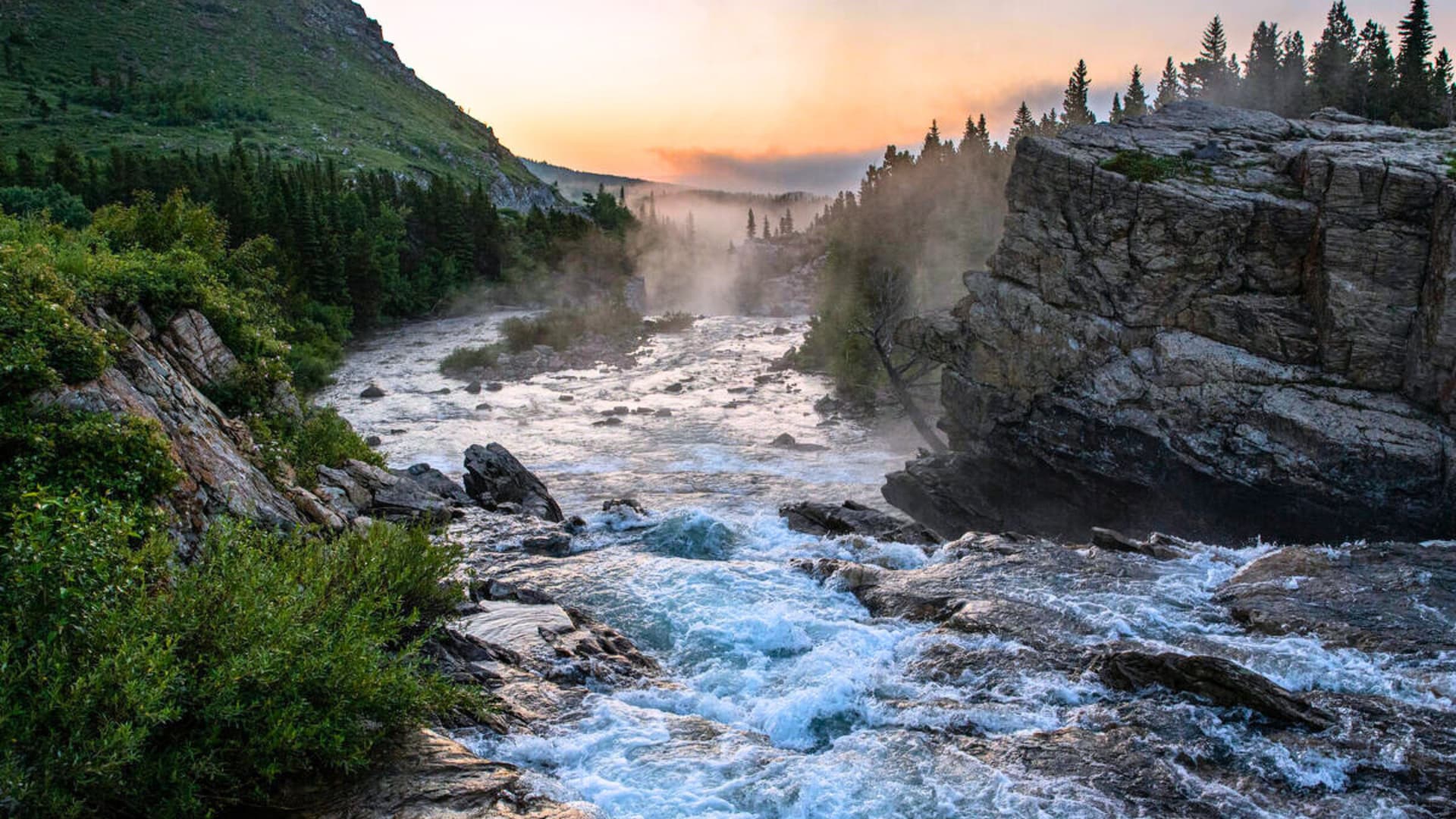 Tauck land tour landscape at Swift Current Lake, Glacier National Park with misty river, forest cliffs, and sunrise glow