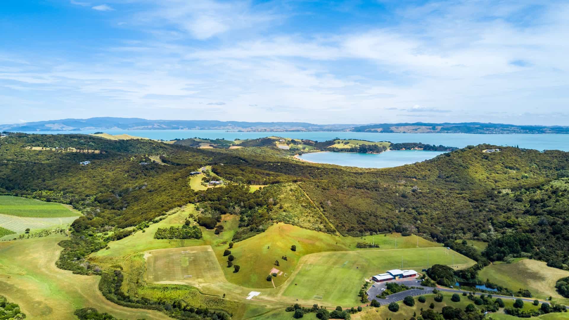 Aerial shot of Waiheke Island in New Zealand showcasing its lush fields, hills, and blue skies.