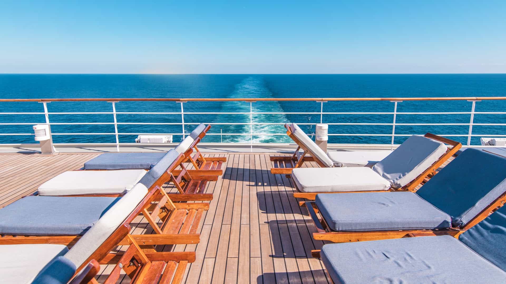 Two rows of lounge chairs on a cruise ship deck during a bright, sunny day.