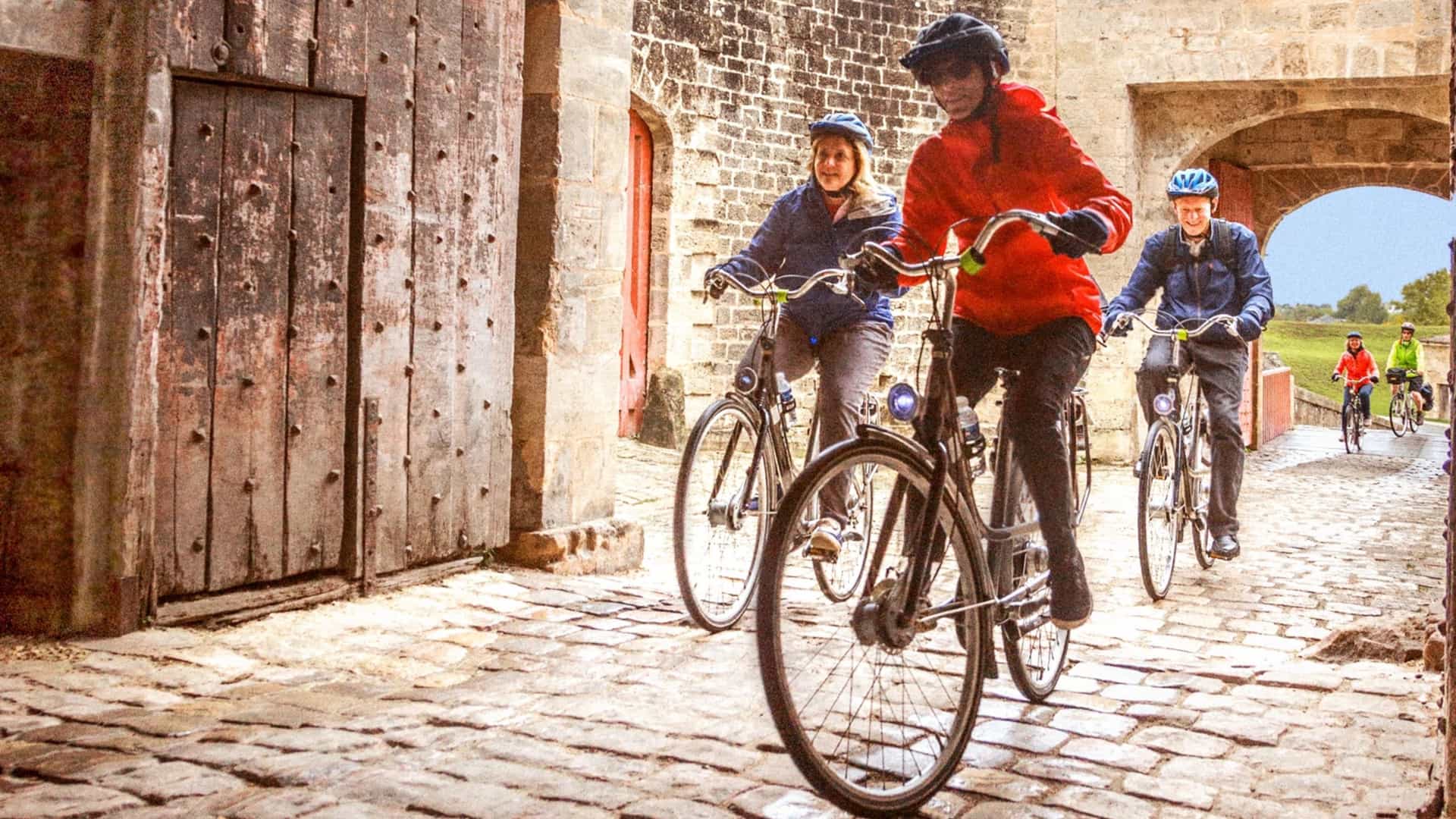AmaWaterways guests enjoy a guided bicycle excursion through a historic cobblestone archway in Bordeaux, France, showcasing the line's included active shore excursions.