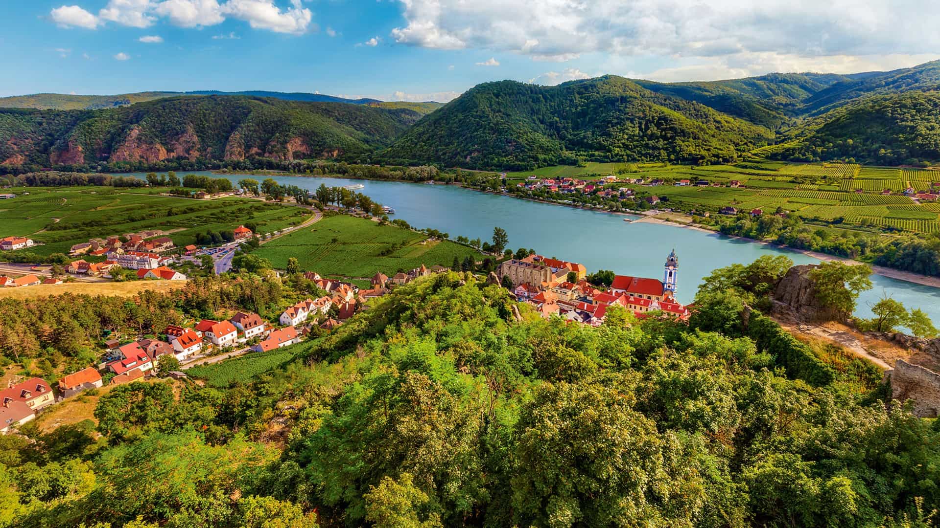 Aerial view of Dürnstein, Austria, on the Danube River, featuring a charming town, vineyards, and green hills, a common AmaWaterways cruise stop.