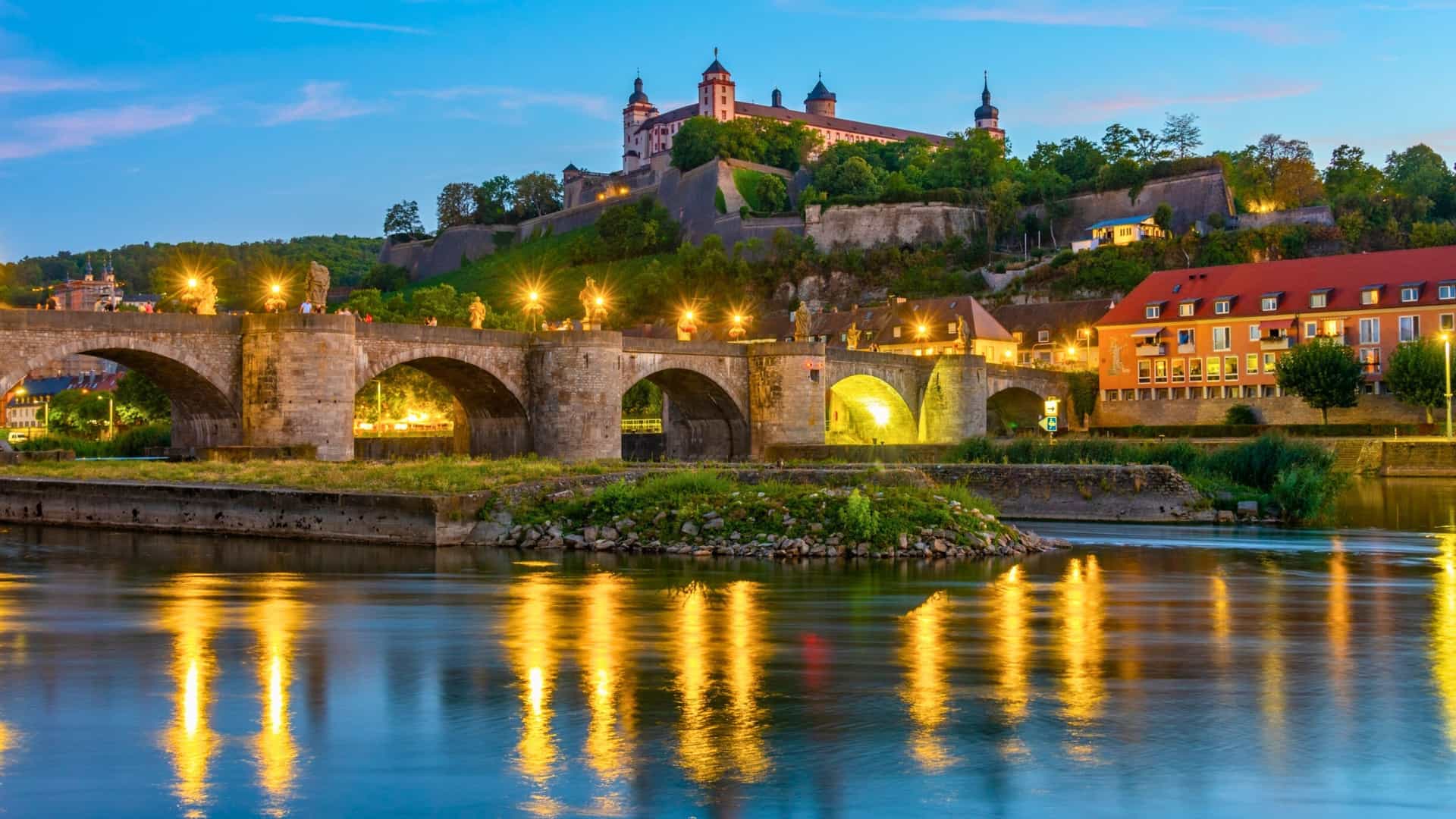AmaWaterways Main River cruise destination in Würzburg, Germany, featuring the illuminated Old Main Bridge and Marienberg Fortress overlooking the river at dusk.