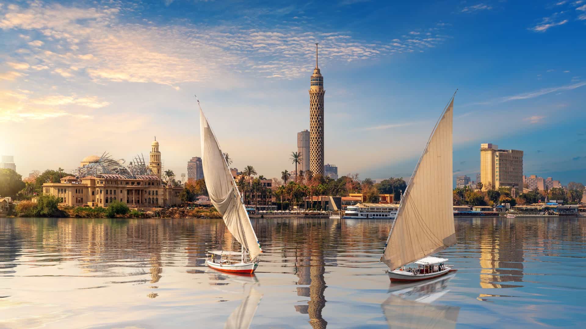 AmaWaterways Nile River cruise on the Egyptian Nile River in Cairo, Egypt, featuring traditional felucca sailboats on the water with the iconic Cairo Tower and city skyline at sunset.