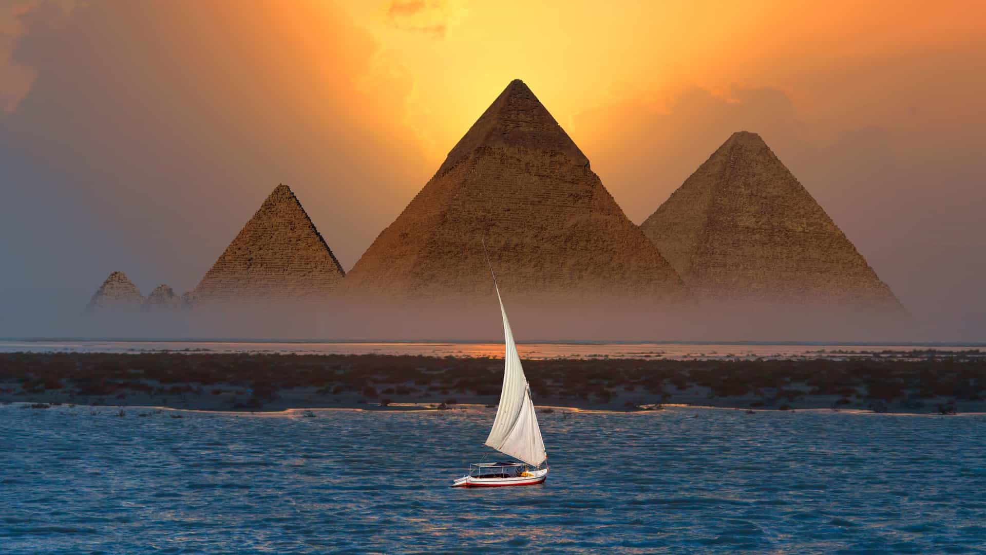 AmaWaterways Nile River cruise excursion in Giza, Egypt, showcasing the majestic Pyramids of Giza at sunset with a traditional felucca sailboat on the water.