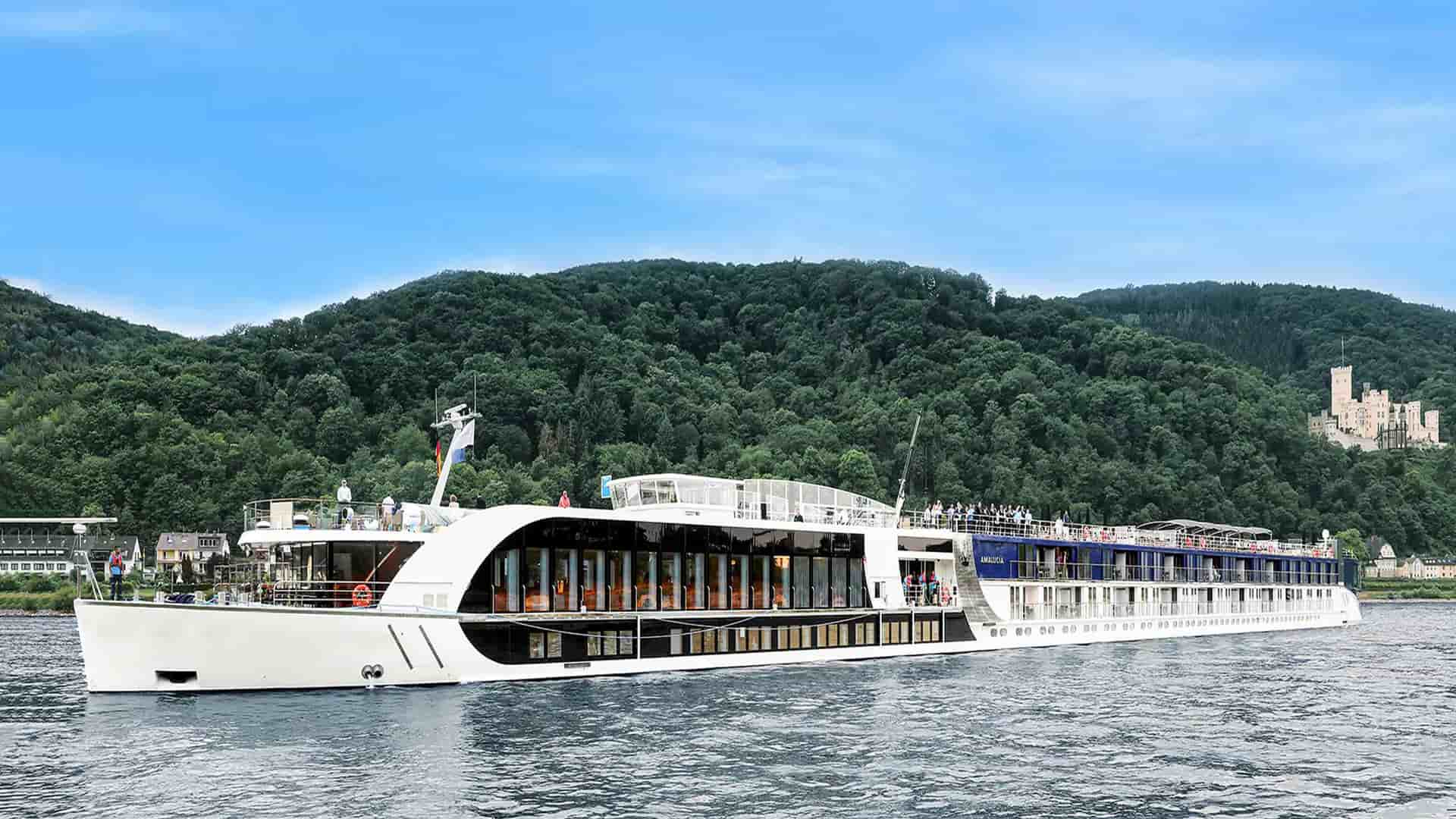 Amawaterways AmaFiora river ship sailing withe luscious green trees and hills in the background.