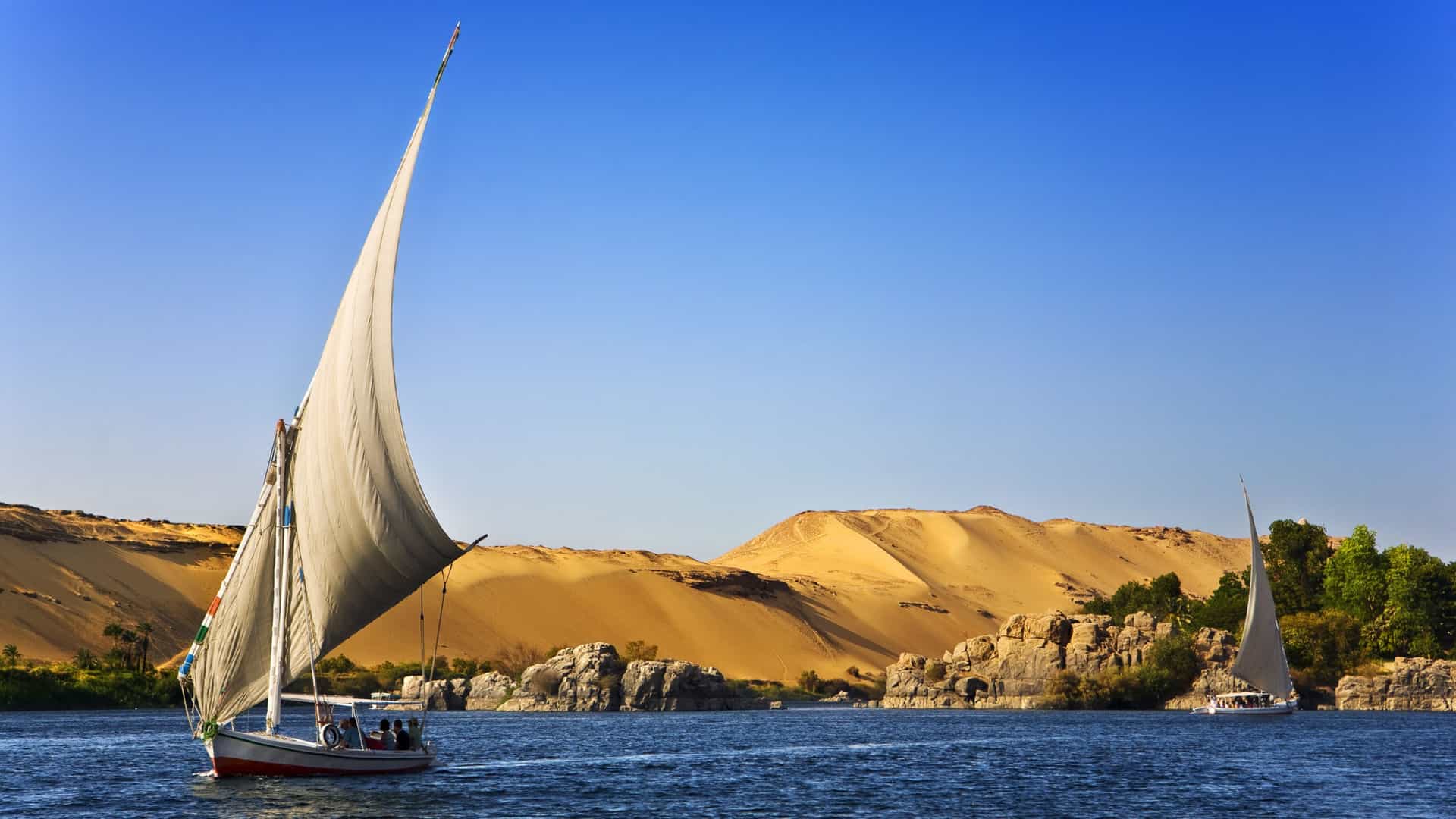 Nile River felucca sailboats with desert dunes, reflecting an Avalon Waterways cultural journey in Egypt.