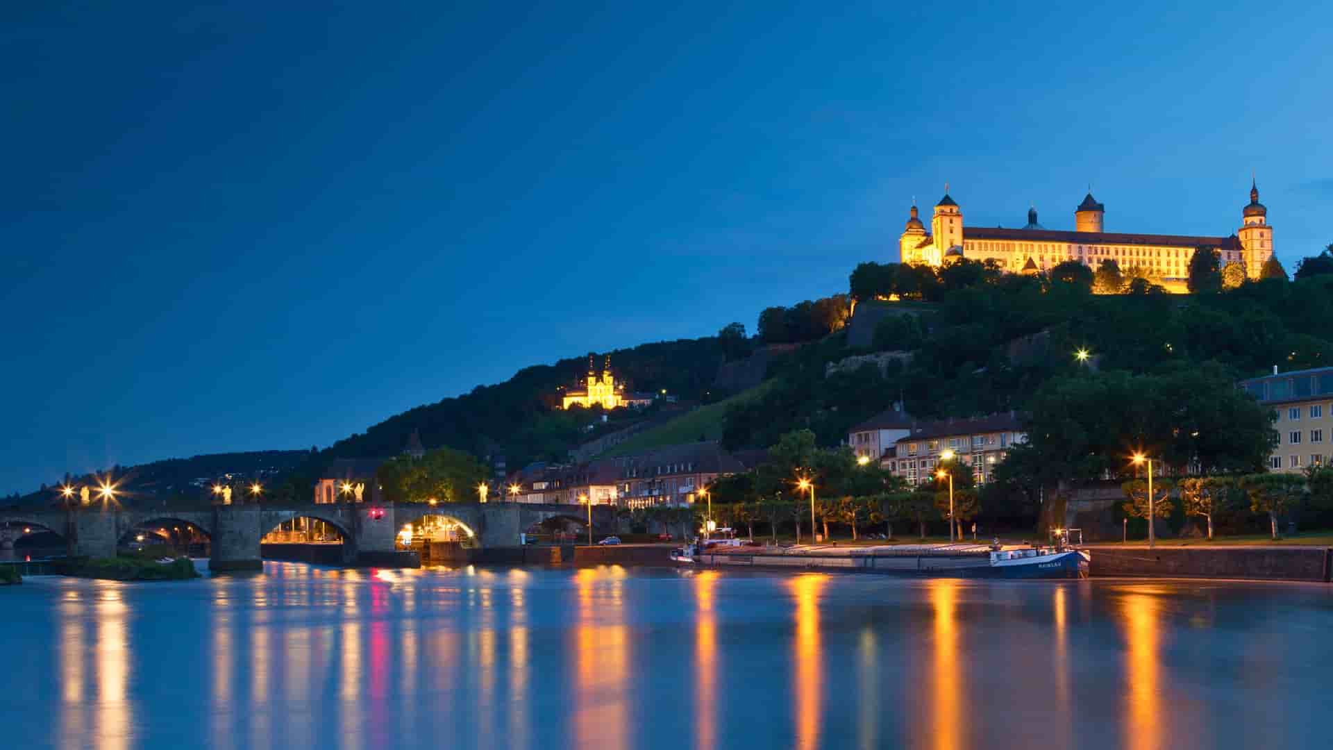 Night view of Würzburg, Germany, with illuminated Fortress Marienberg, Main River, and Old Main Bridge, a charming stop on Avalon Waterways cruises.