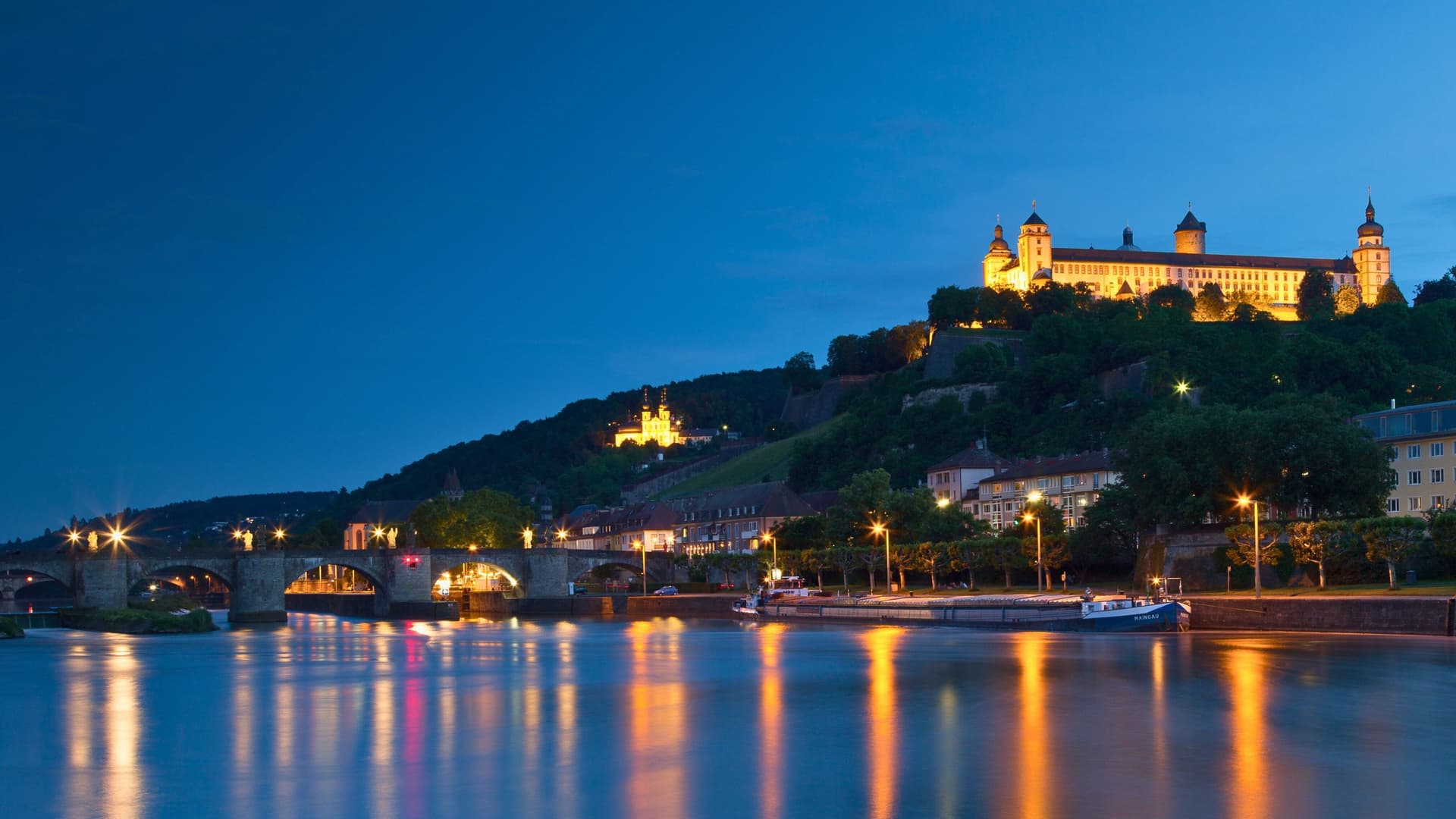 Night view of Würzburg, Germany, with illuminated Fortress Marienberg, Main River, and Old Main Bridge, a charming stop on Avalon Waterways cruises.