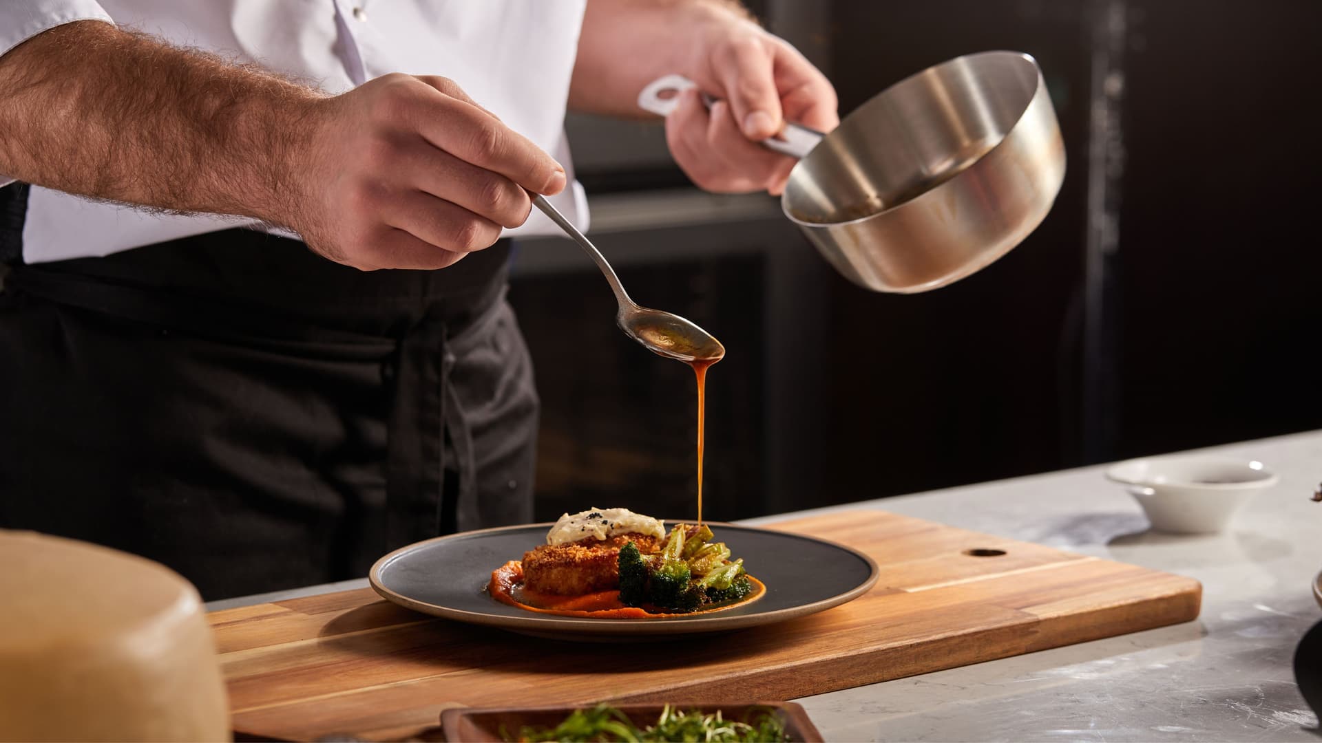 A chef drizzling a sauce on a plated meal before serving to restaurant guests.