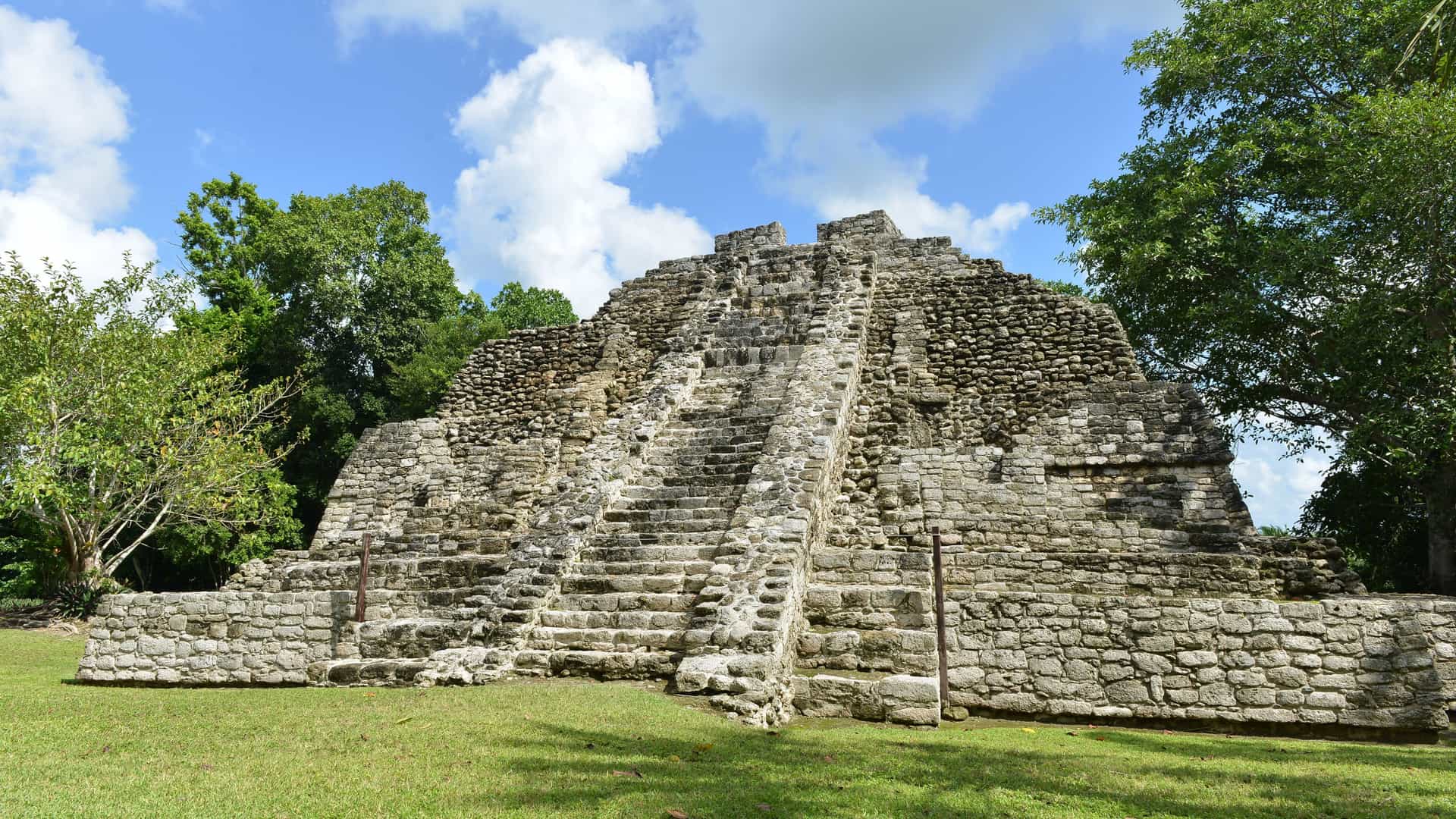 Ancient Mayan ruins surrounded by lush green trees under a blue sky, representing a historical excursion available to Carnival cruise passengers visiting Costa Maya, Mexico.