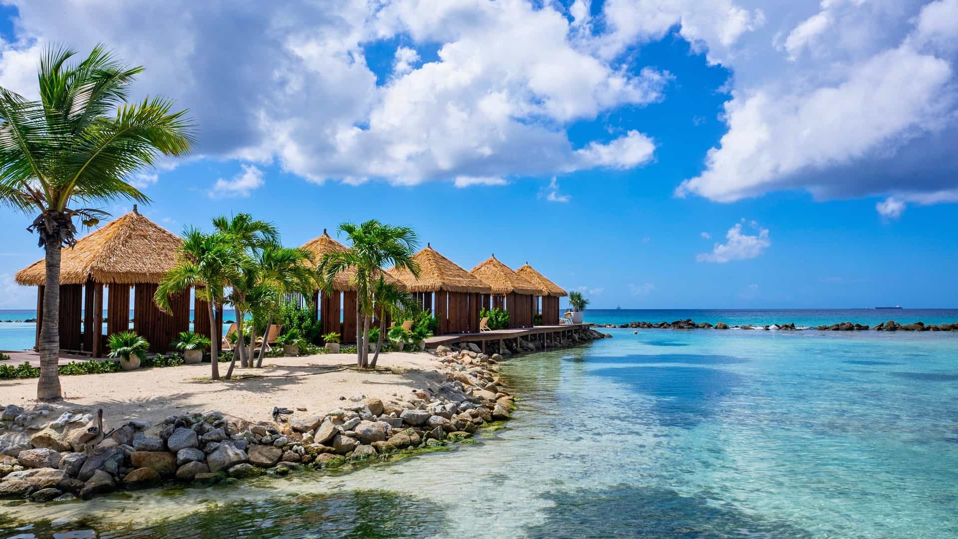 Aruba's picturesque beach with tranquil turquoise waters and charming straw cabanas, a popular stop for Carnival Southern Caribbean cruises.