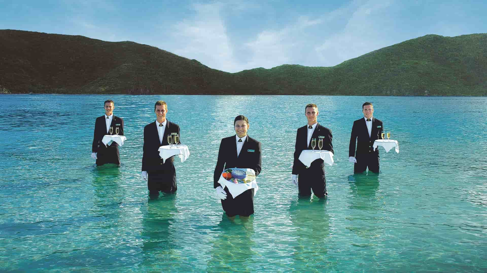 Five members of Seabourn's staff in suits standing in the water holding trays for the signature Caviar in the Surf event.
