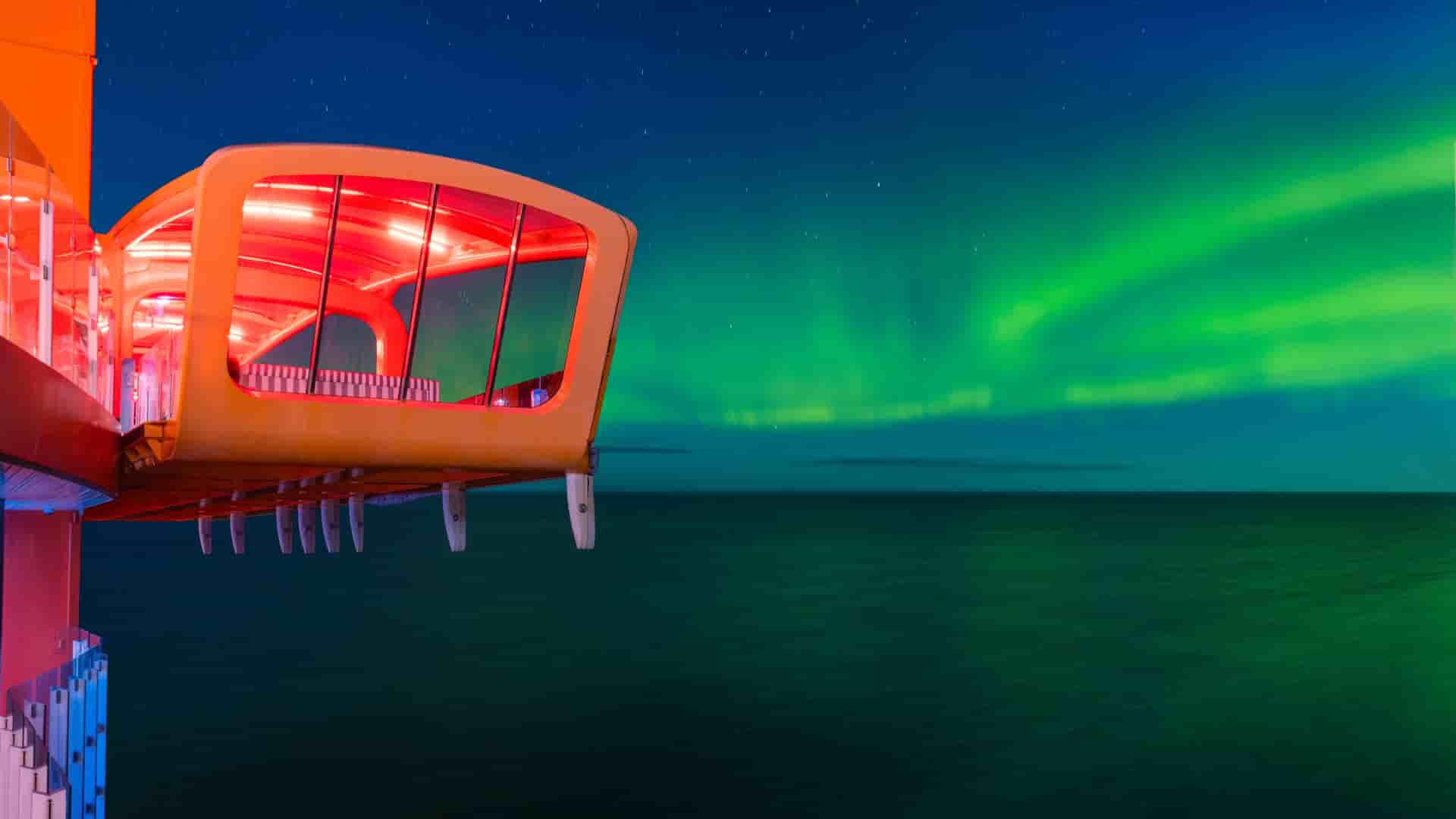 The Magic Carpet on Celebrity Edge cantilevers over dark Arctic waters beneath a brilliant display of the northern lights.