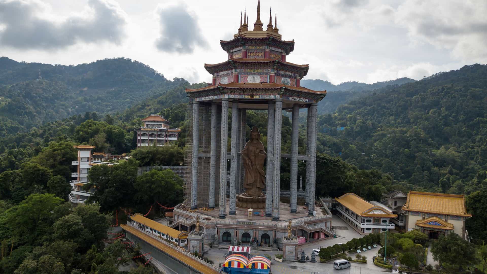 The giant Kuan Yin statue and pagoda pavilion at Kek Lok Si Temple in Penang, Malaysia, set against forested hills.