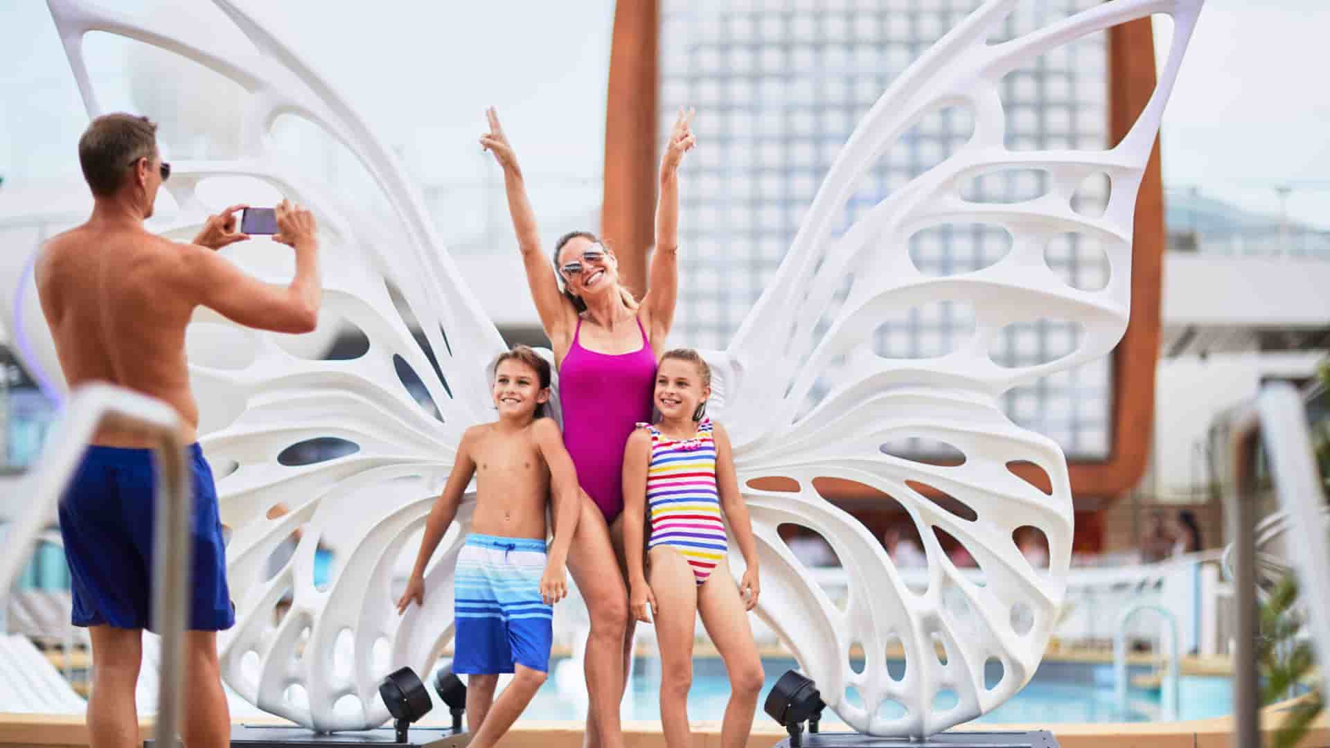 A family posing for a fun photo in front of a butterfly sculpture poolside on the Celebrity Edge cruise ship.