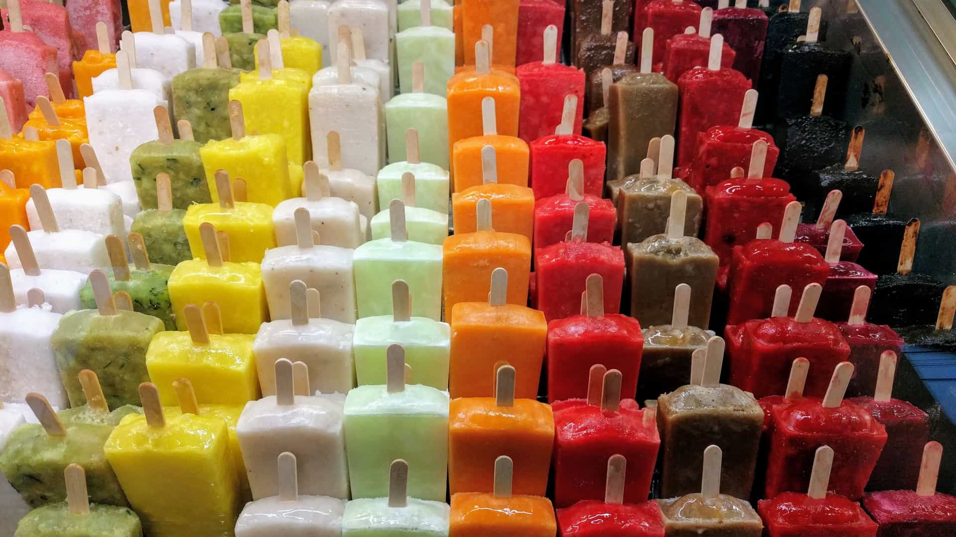 An array of different flavors of Mexican paletas stacked neatly in a freezer display.