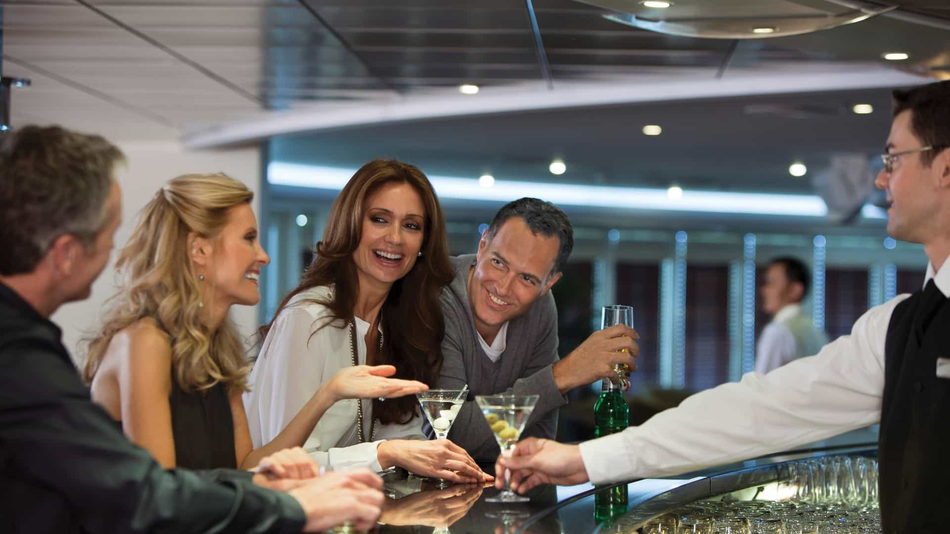 Two couples laughing and getting drinks together on a Regent Seven Seas' ship lounge.